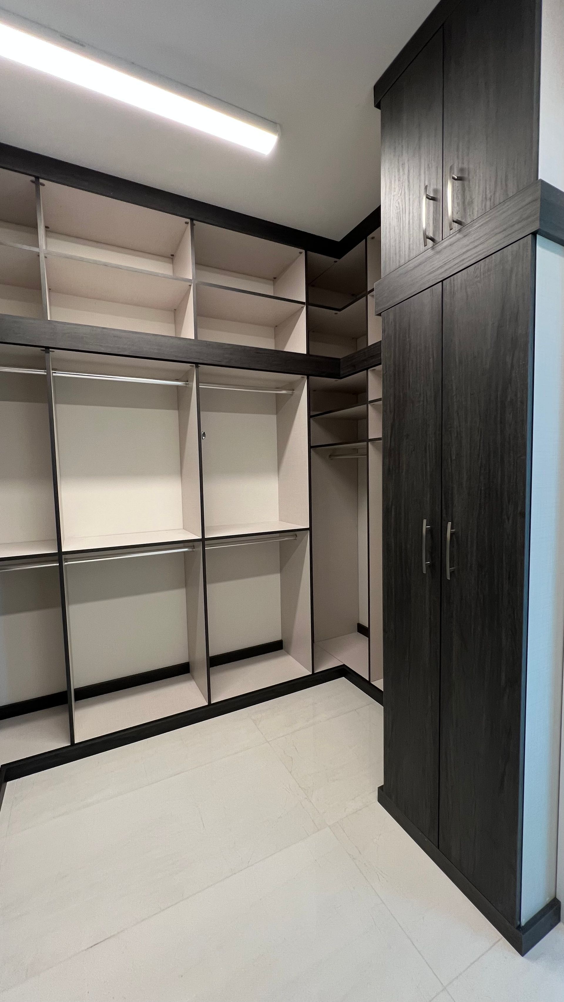 Modern walk-in closet featuring light-toned open shelving, hanging rods, and a dark wood floor-to-ceiling cabinet.