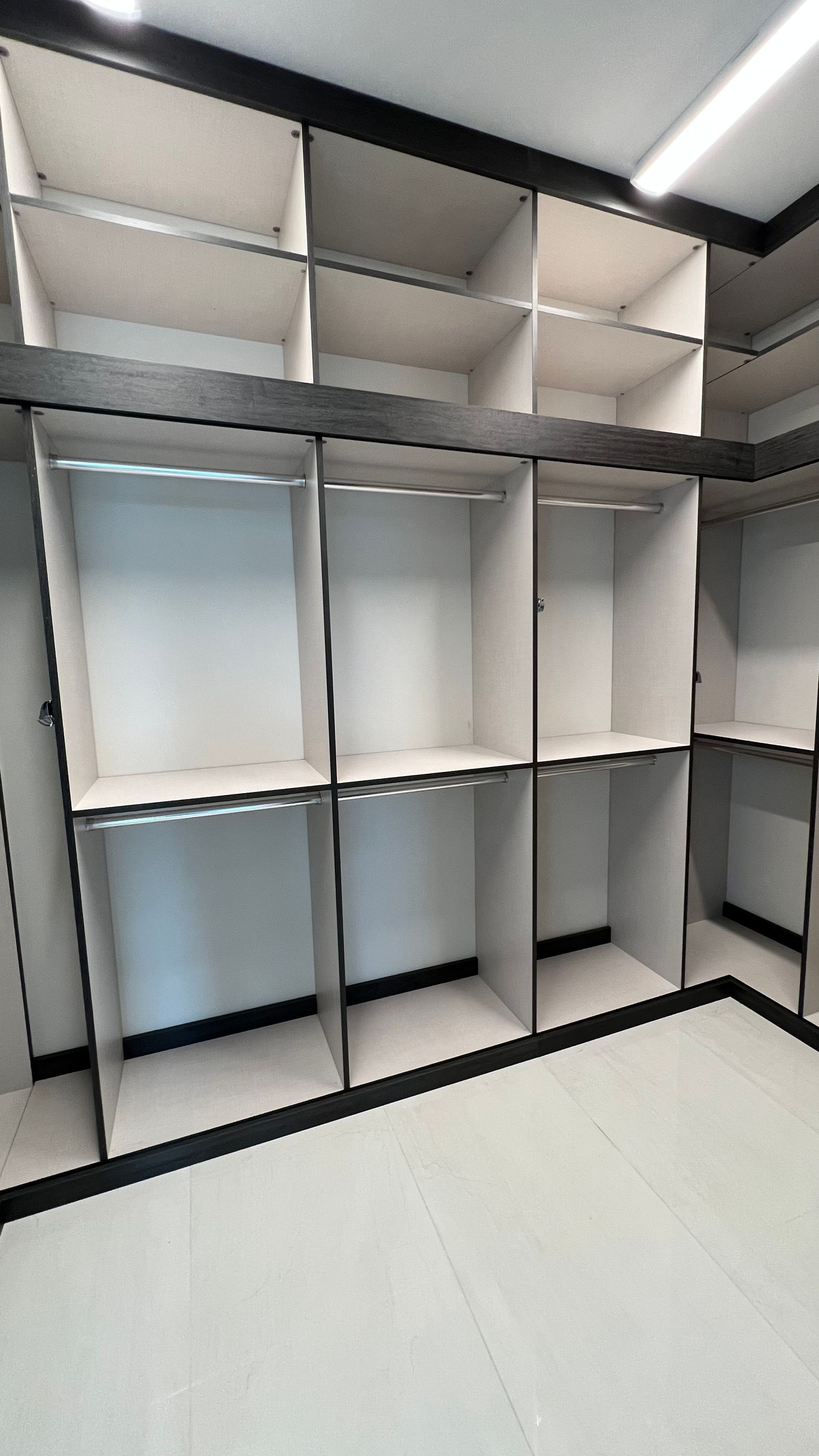 A view into an empty walk-in closet with white shelving, dark wood trim, and a bright overhead light.
