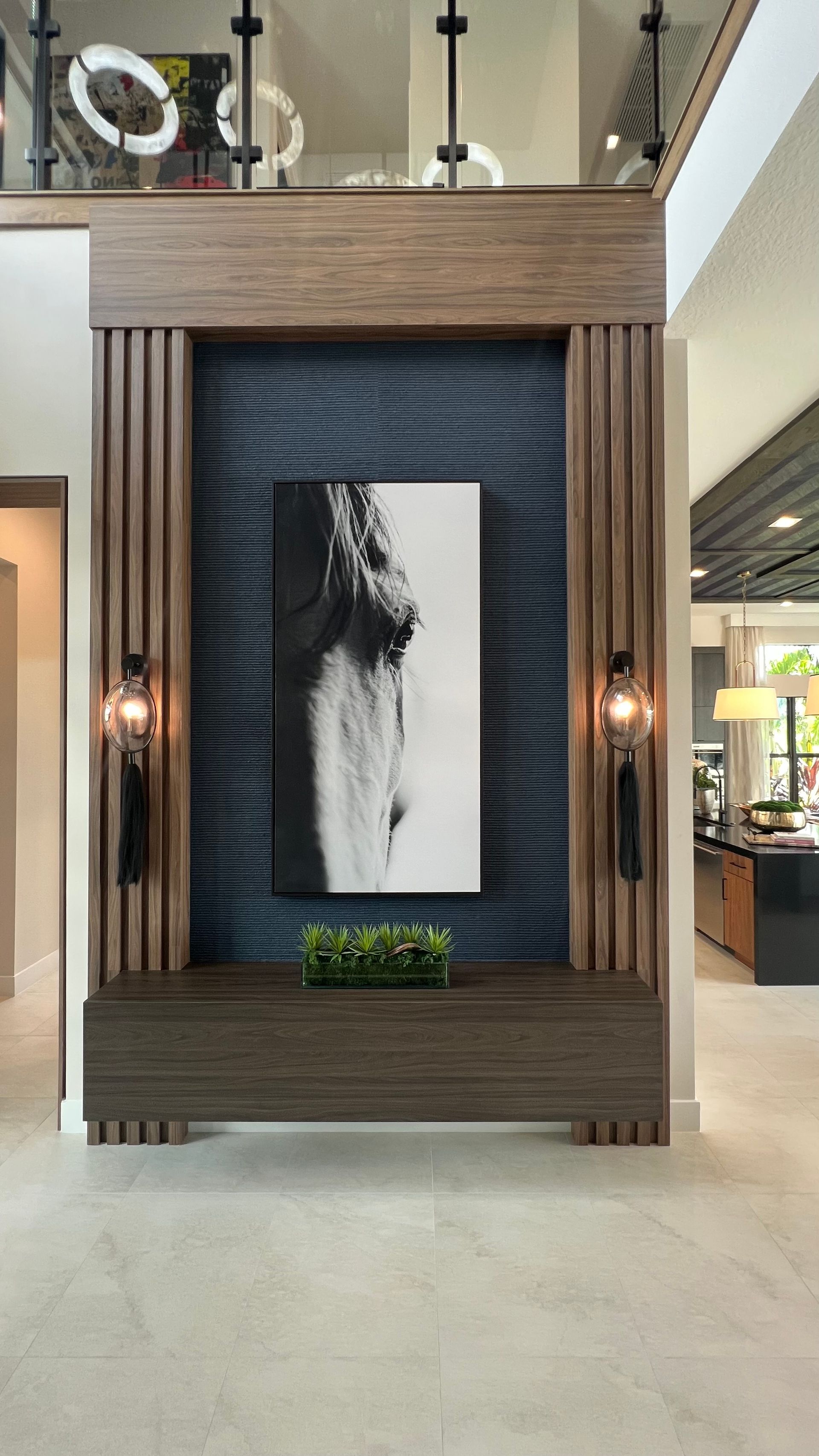 A modern home foyer with a dark wood-paneled niche, textured blue backdrop, framed abstract art, and wall sconces.