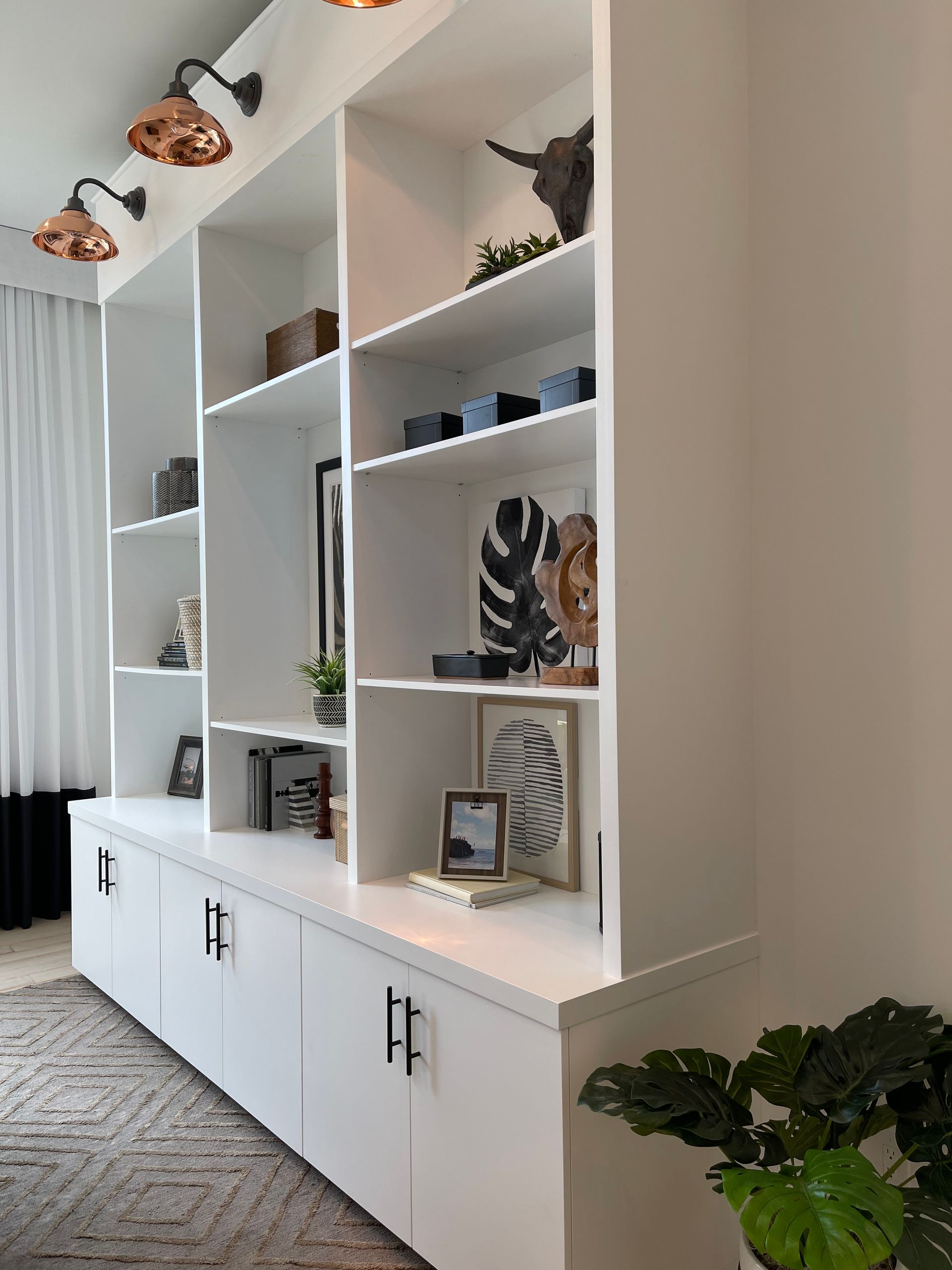 A white, floor-to-ceiling built-in bookcase featuring shelving and lower cabinets with dark metal hardware.