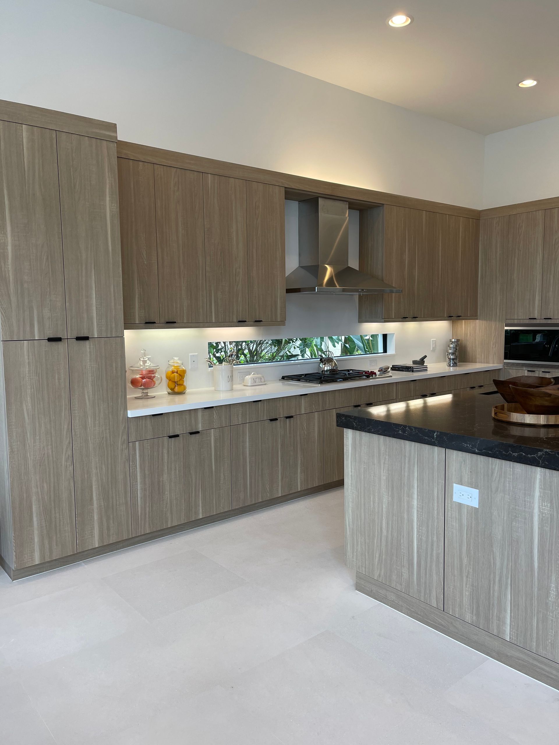 Modern kitchen with light wood-grained cabinets, white countertops, a horizontal window backsplash, and a dark island.