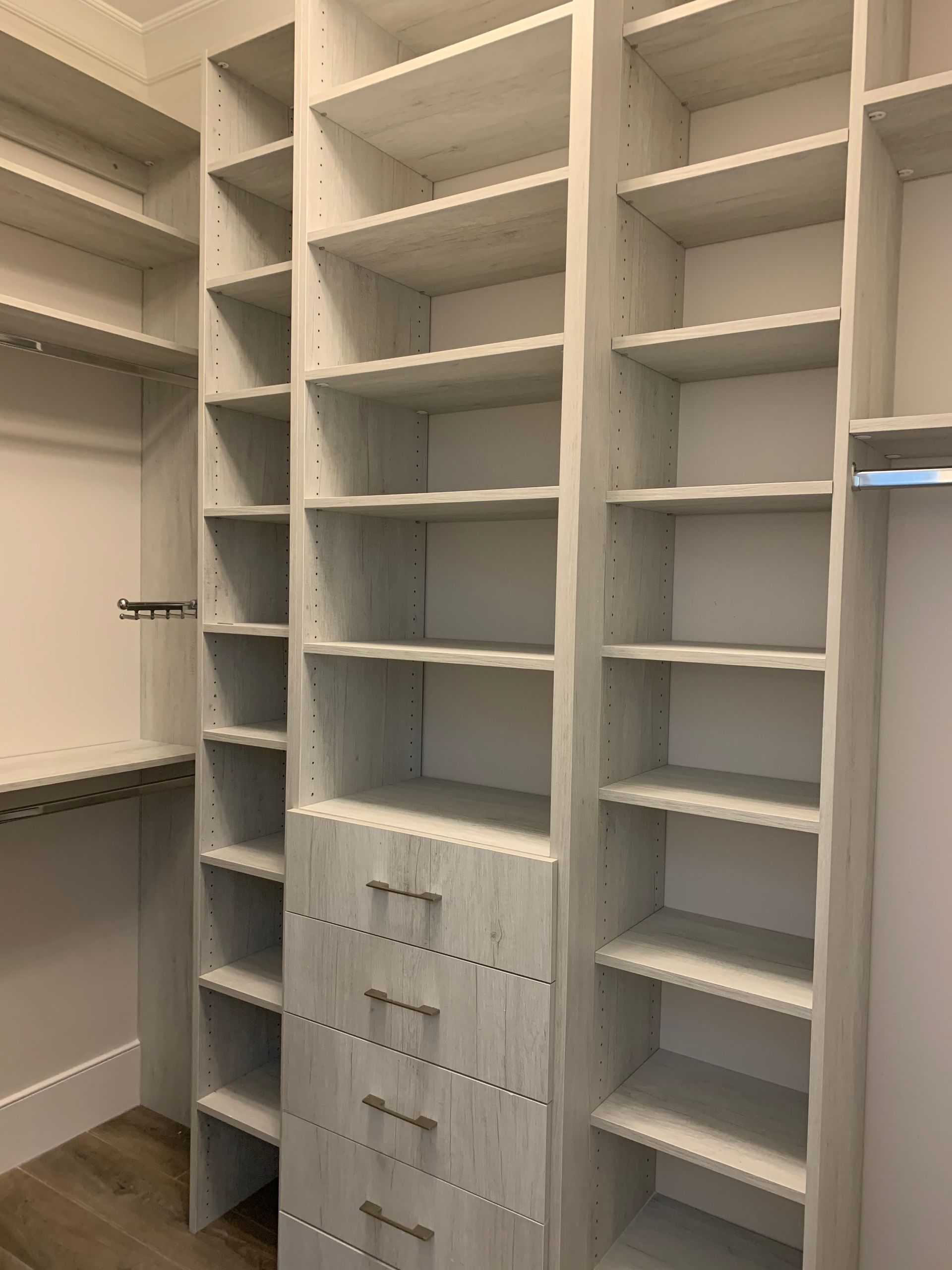 A walk-in closet with light-wood finish shelving, including narrow vertical shelves and a central stack of four drawers.