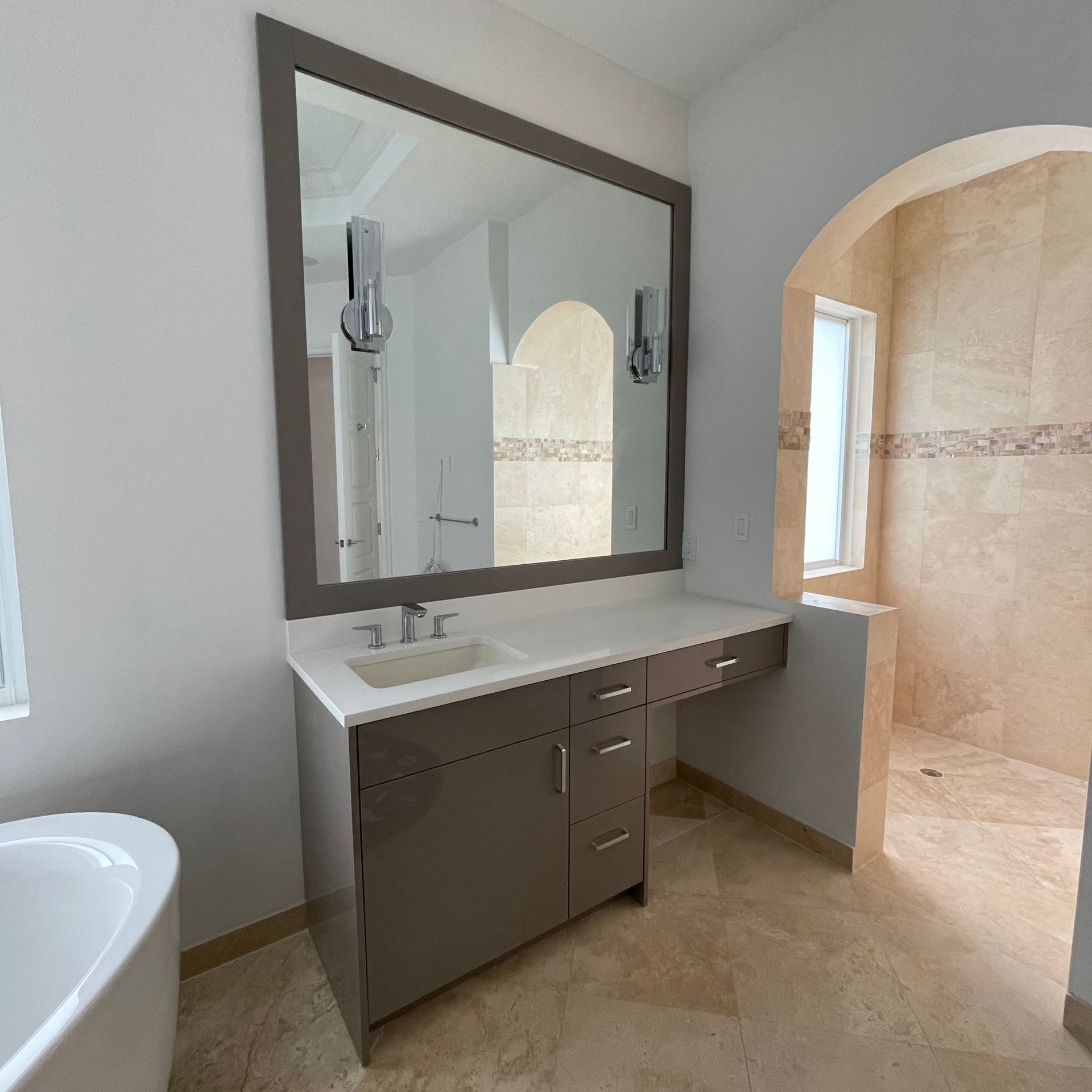 A bathroom vanity with a large mirror, gray cabinets, a white countertop, and a walk-in shower with tiled walls.