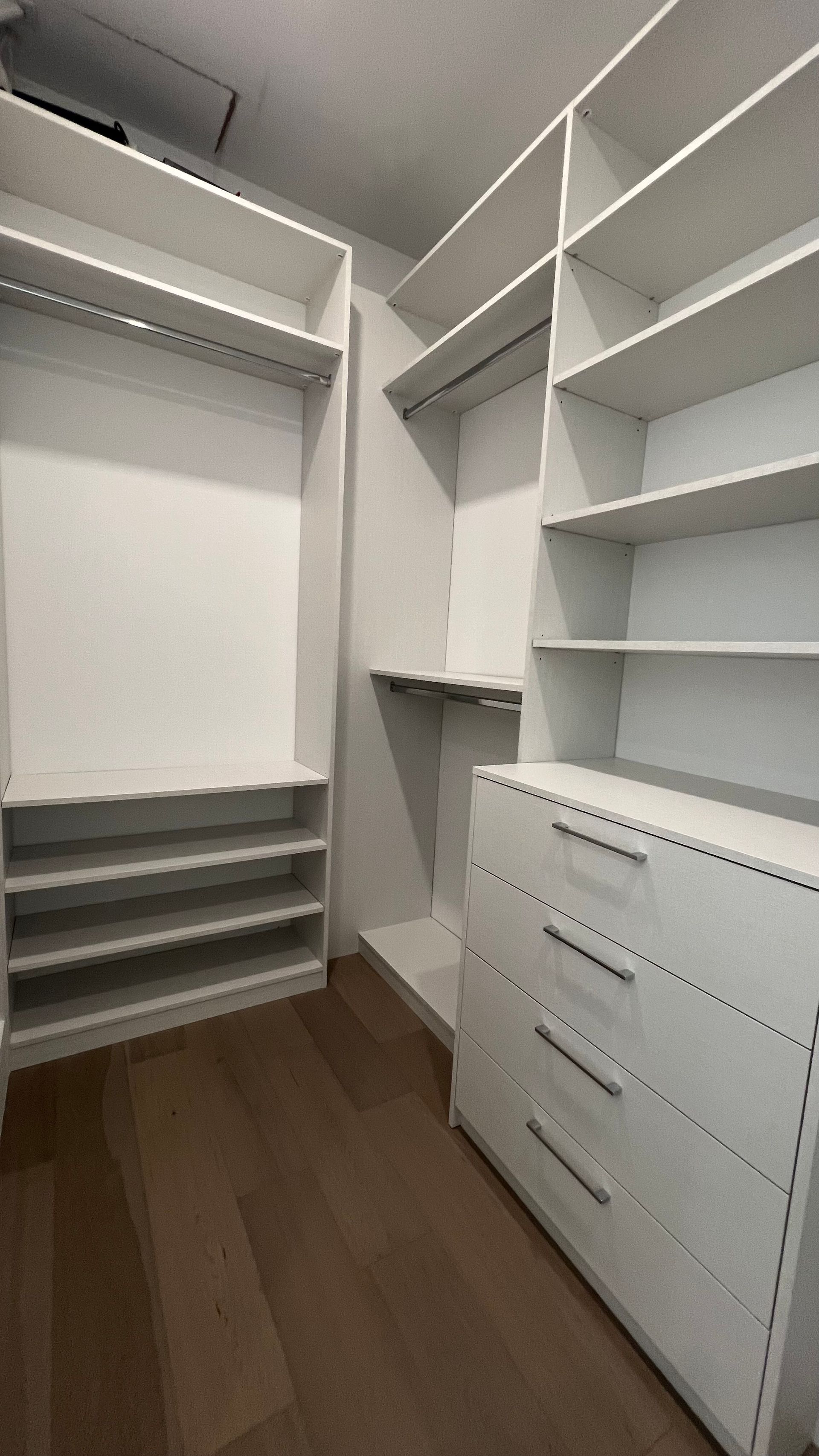 A walk-in closet featuring white wooden shelving, a hanging rod, a four-drawer dresser, and light brown wood-plank flooring.