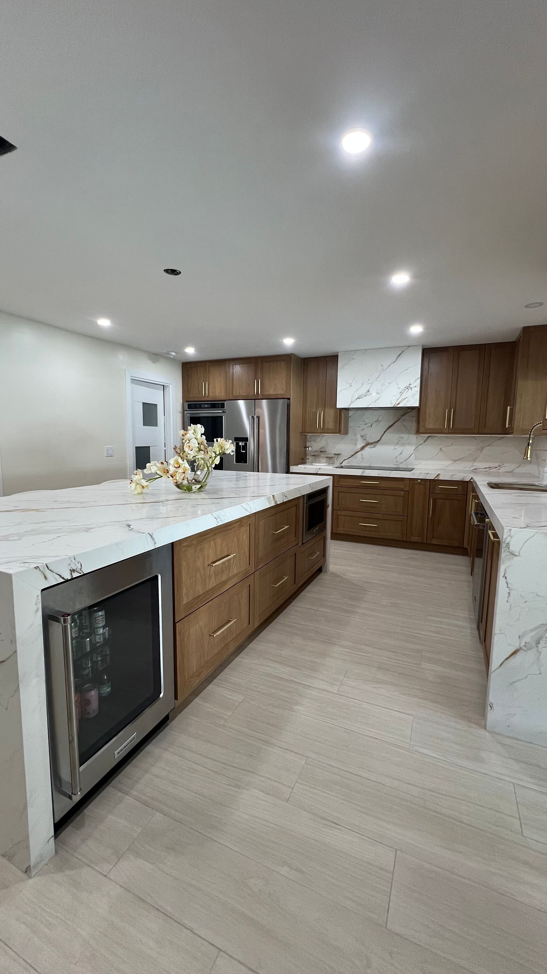 Modern kitchen with warm wood cabinets, a large white marble island with a wine fridge, and marble backsplash.