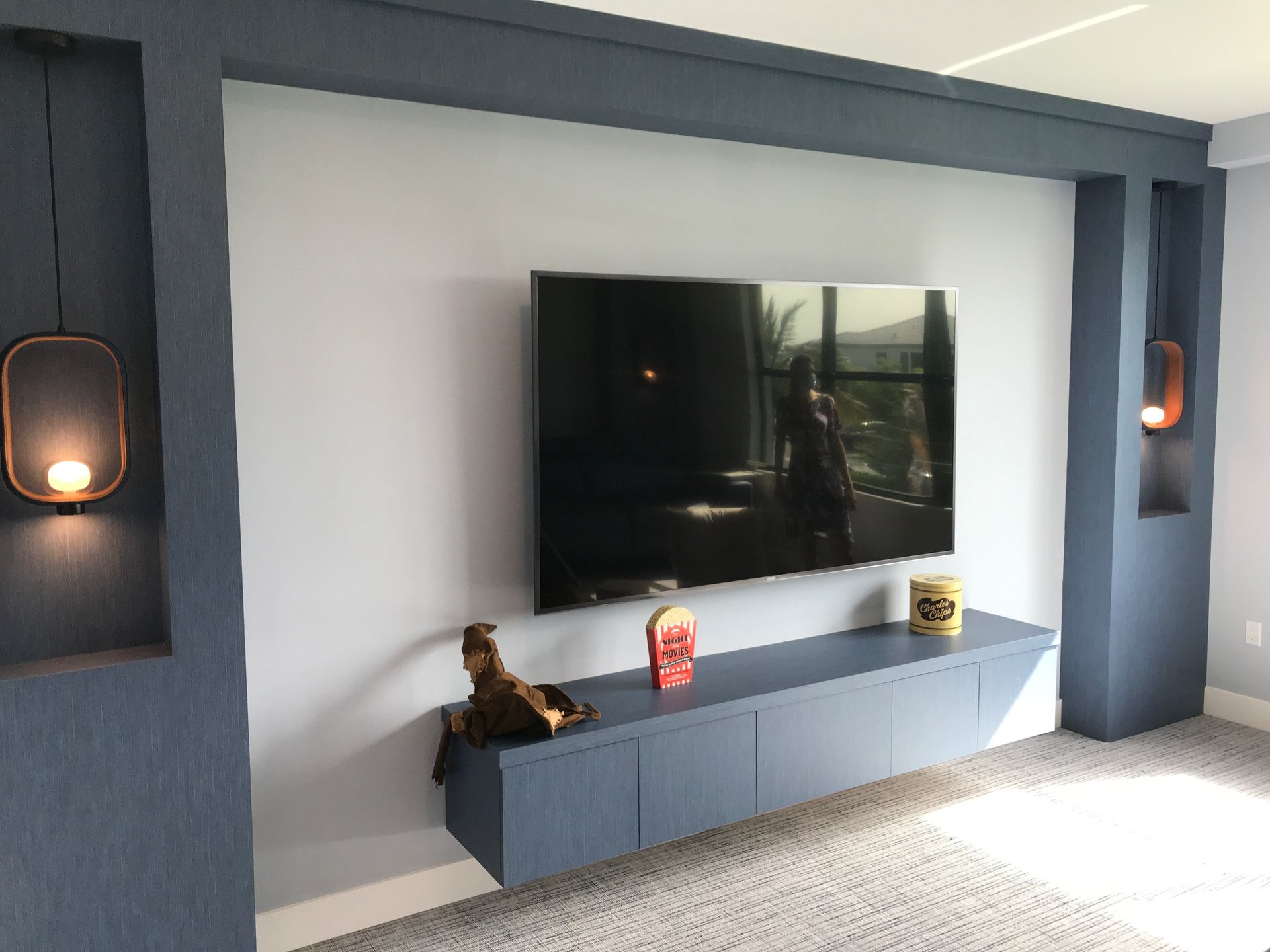 A wall-mounted TV sits above a floating blue console, flanked by two navy-blue alcoves with integrated warm lighting.