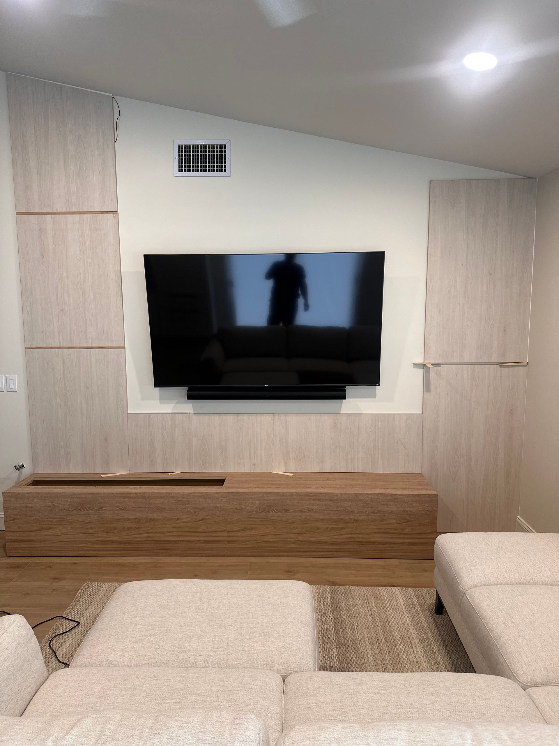 A wall-mounted TV and soundbar centered above a low wooden media console in a room with light-colored, paneled accent walls.