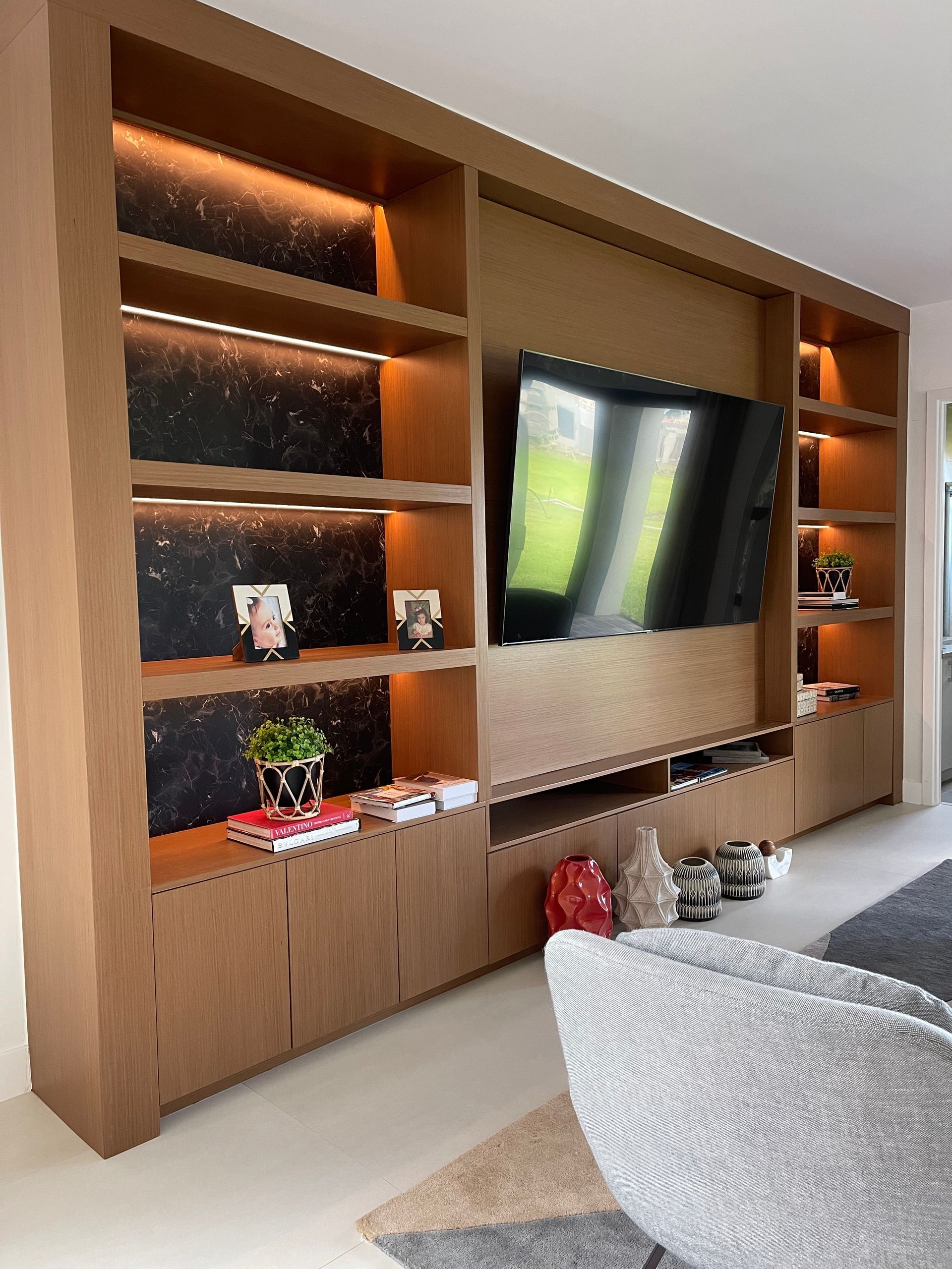 A large, light-wood media wall with open shelving and a wall-mounted TV, featuring black patterned back panels and LED lights.