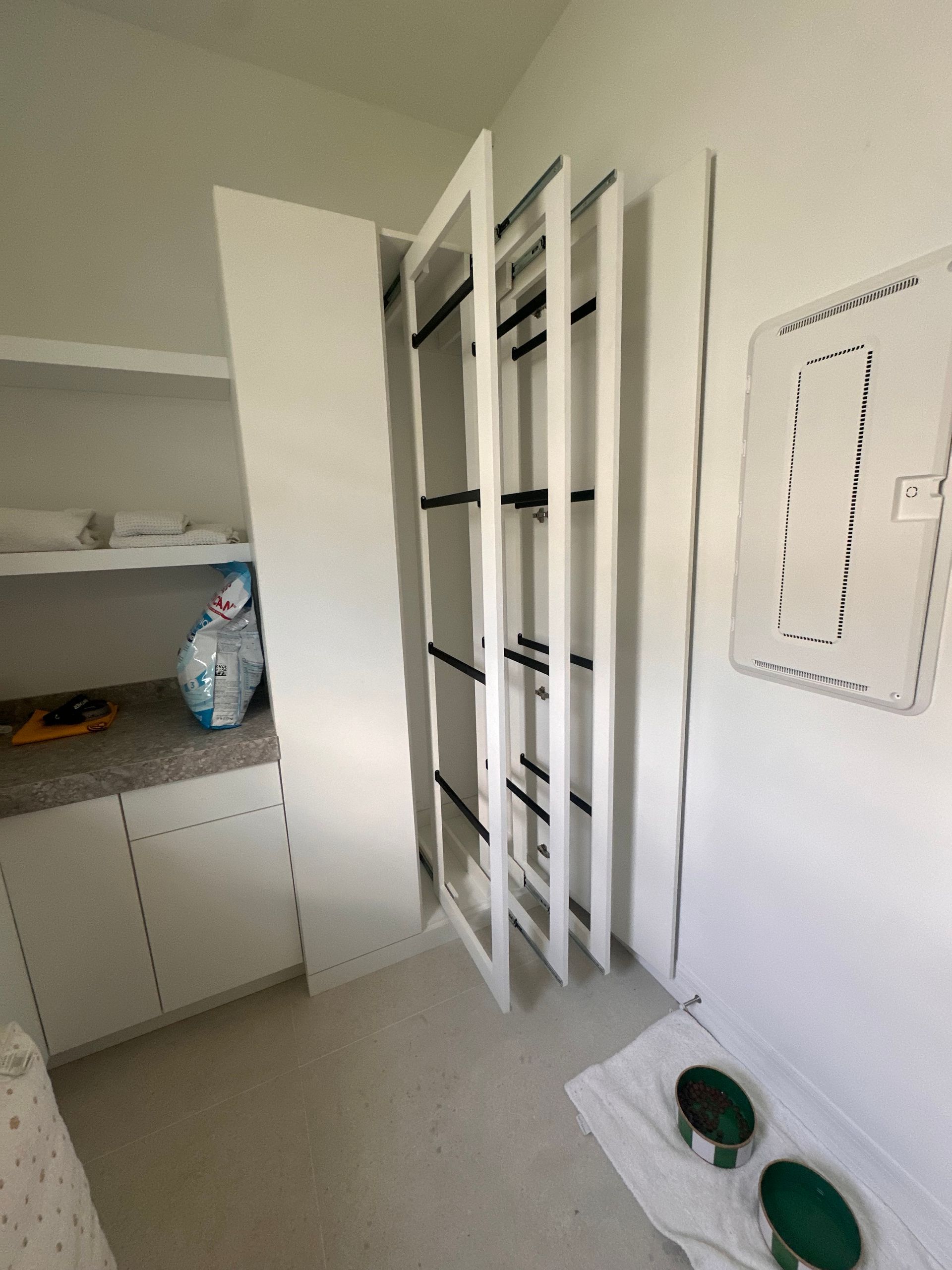 White vertical pull-out pantry shelves stand partially extended in a bright kitchen with white cabinets and tiled floors.