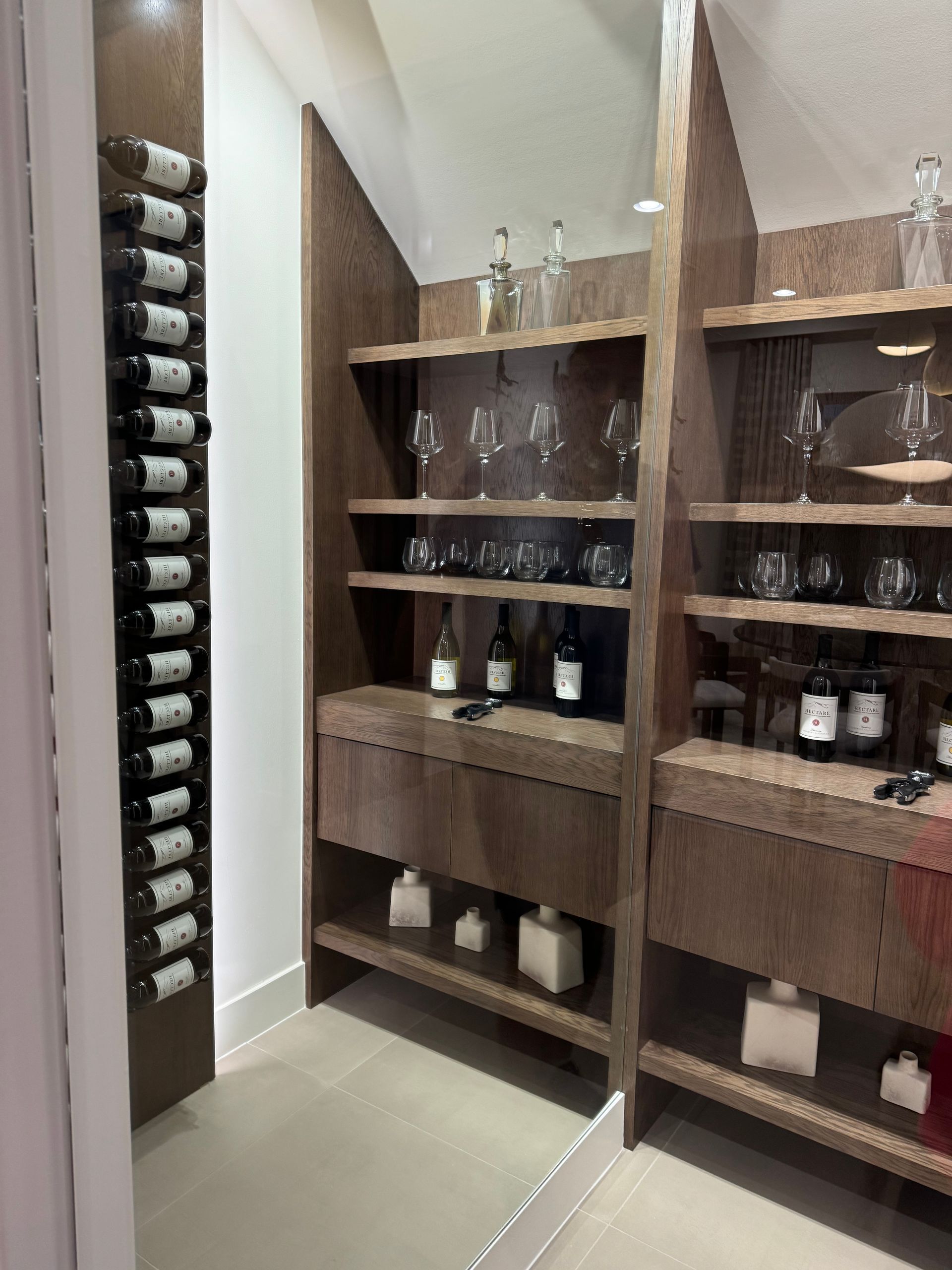Custom wooden wine cellar featuring a wall-mounted rack, open shelves with glassware and bottles, and lower cabinets.
