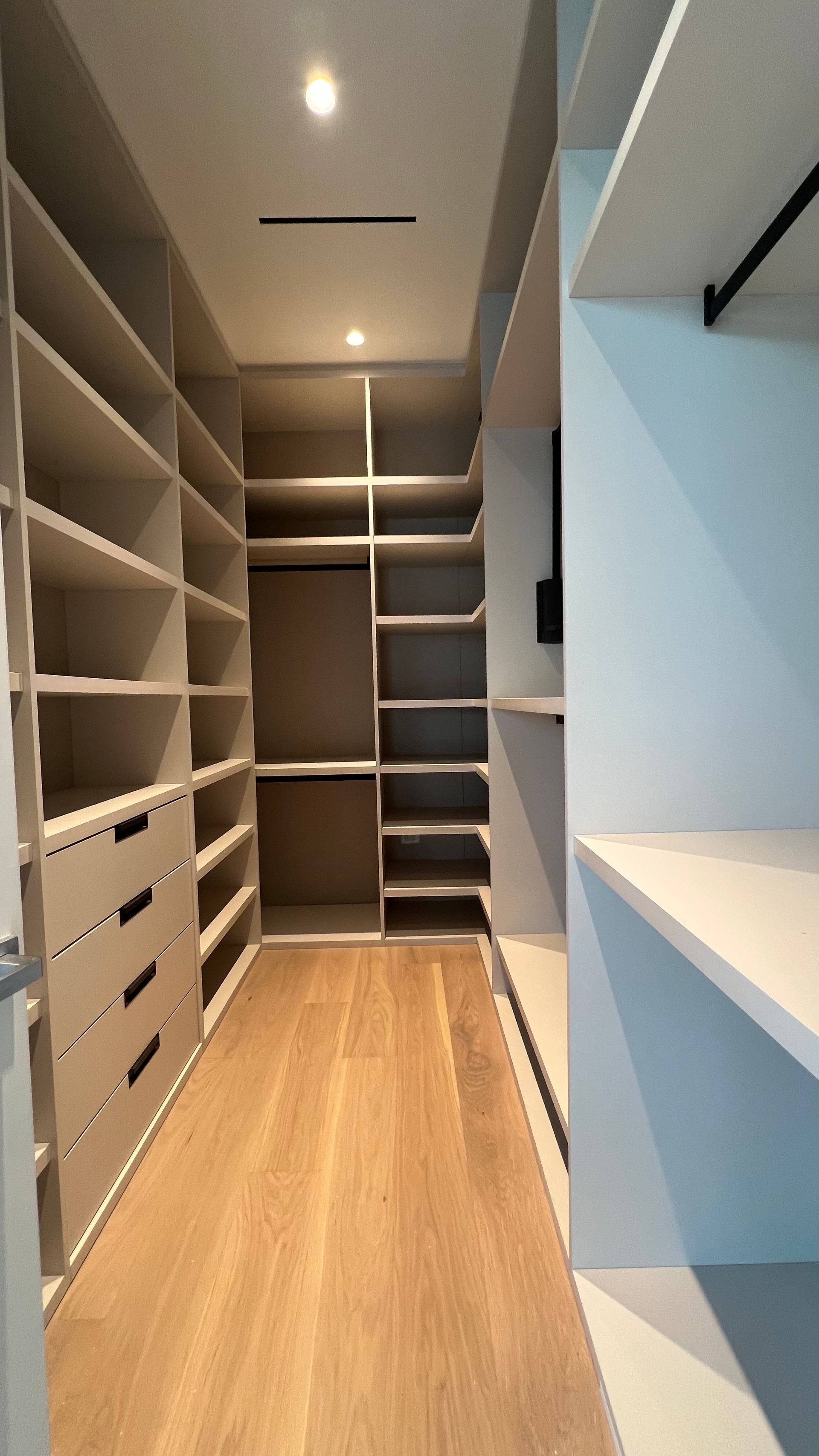 A walk-in closet featuring light-colored wooden shelving, drawers, and a light wood-tone floor under recessed lighting.