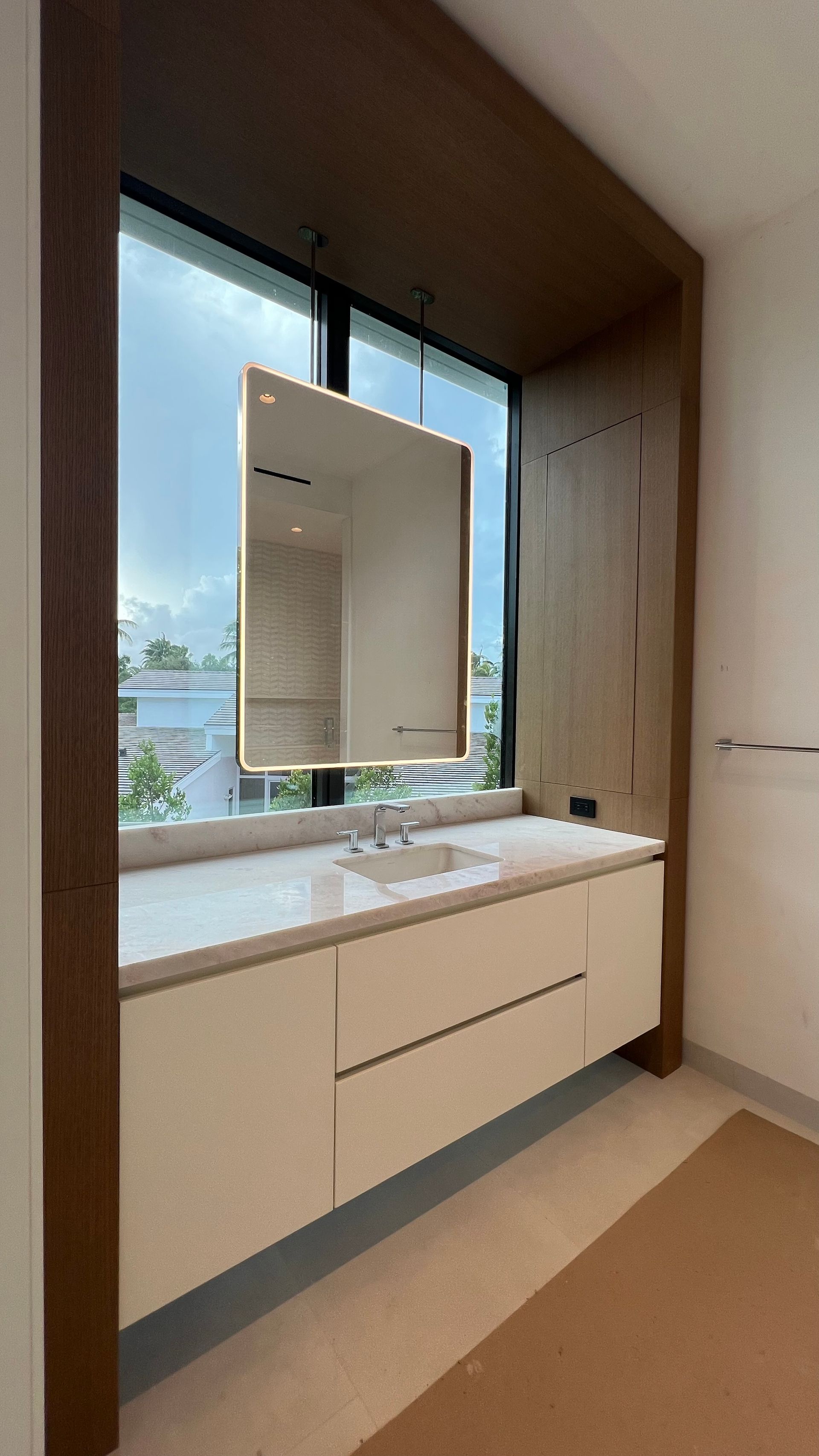 Modern bathroom vanity with cream cabinets, white countertop, and a suspended mirror in front of a window.