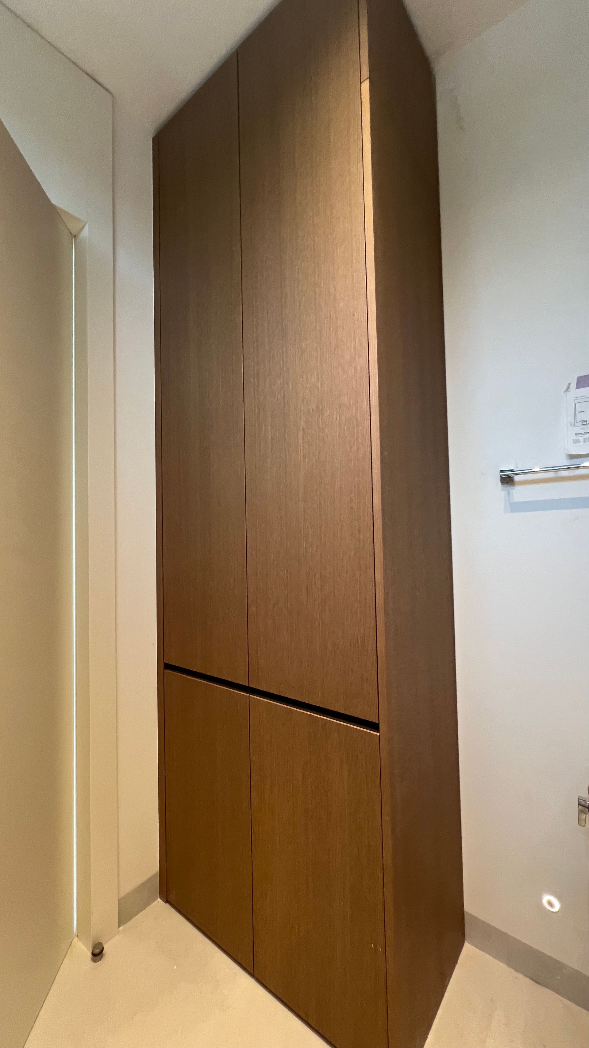 A tall, dark brown, four-door storage cabinet situated in the corner of a room with white walls and flooring.