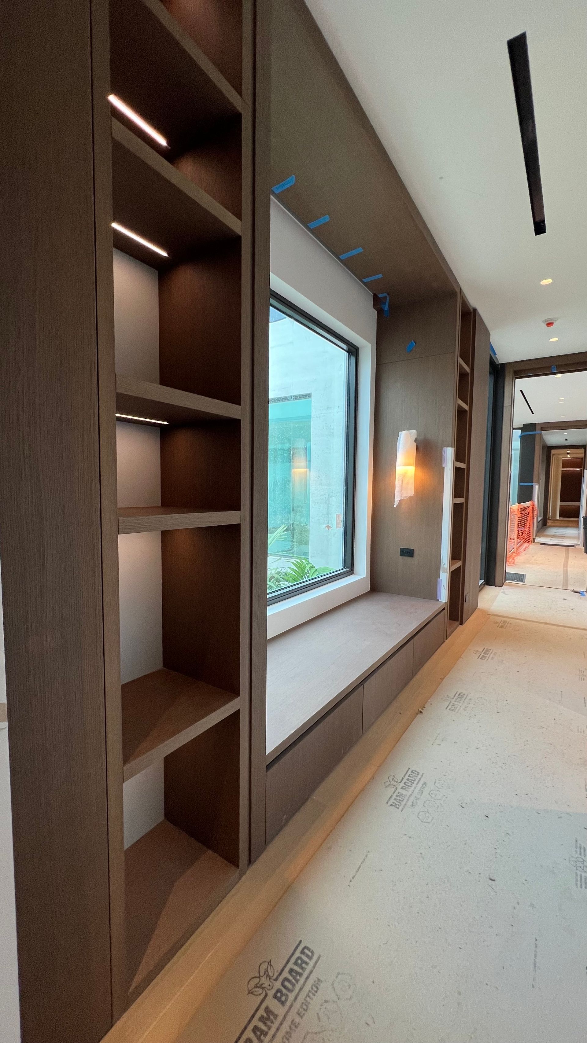A window seat with integrated wooden shelving and warm accent lighting in a room under construction.