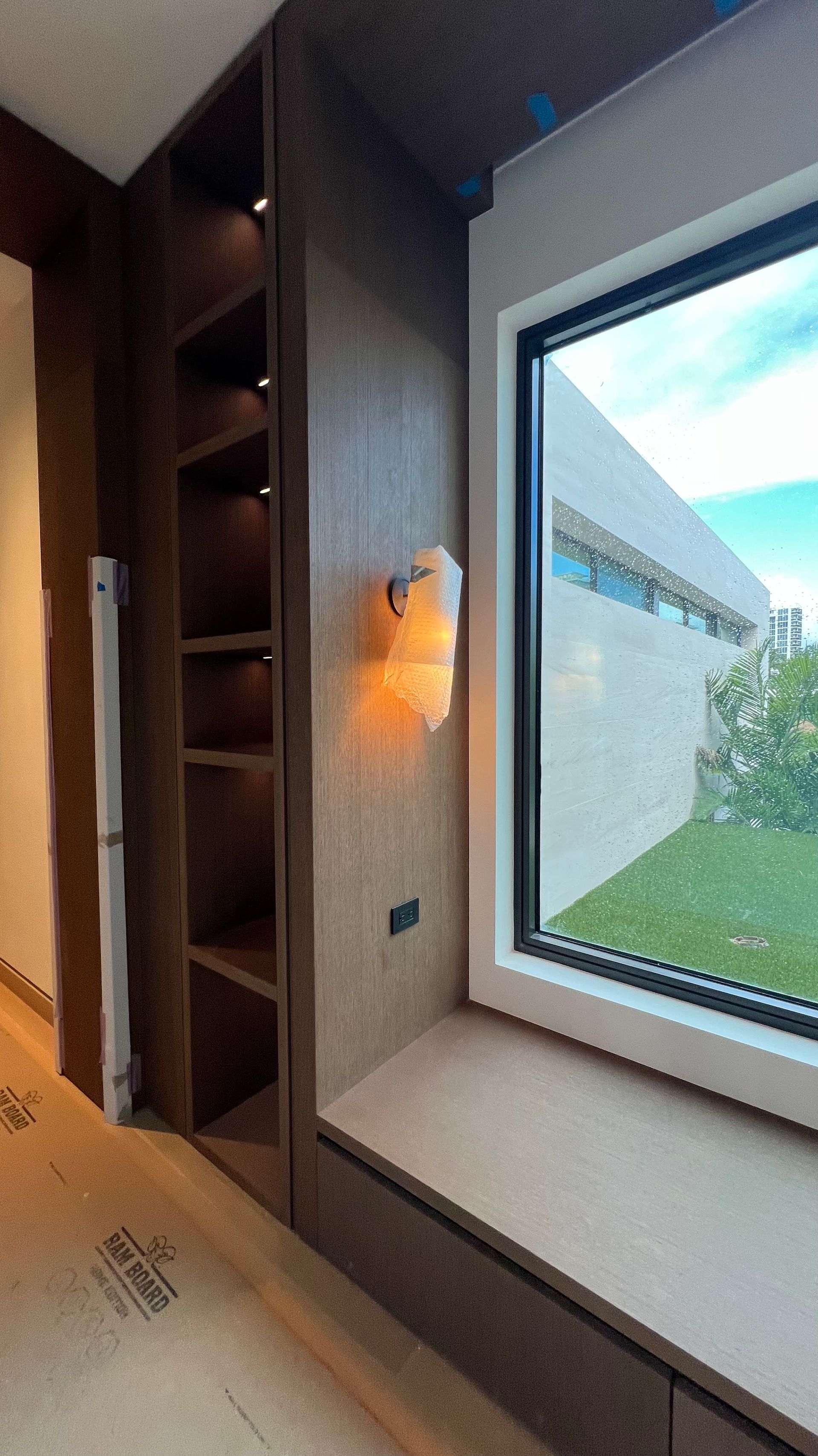 A recessed wooden shelving unit next to a window seat with a wall-mounted light fixture, viewed during construction.