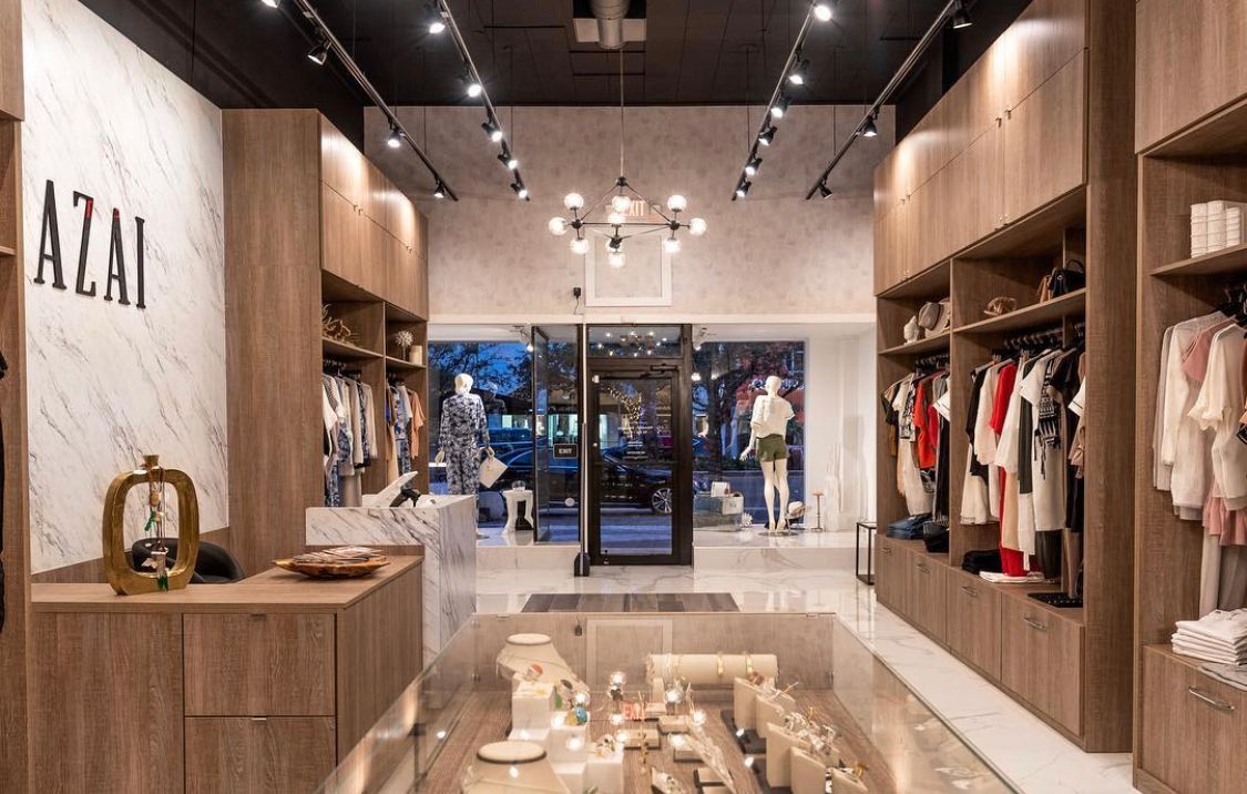 A modern boutique interior with wood shelving, white marble accents, hanging clothing, and a central jewelry display.