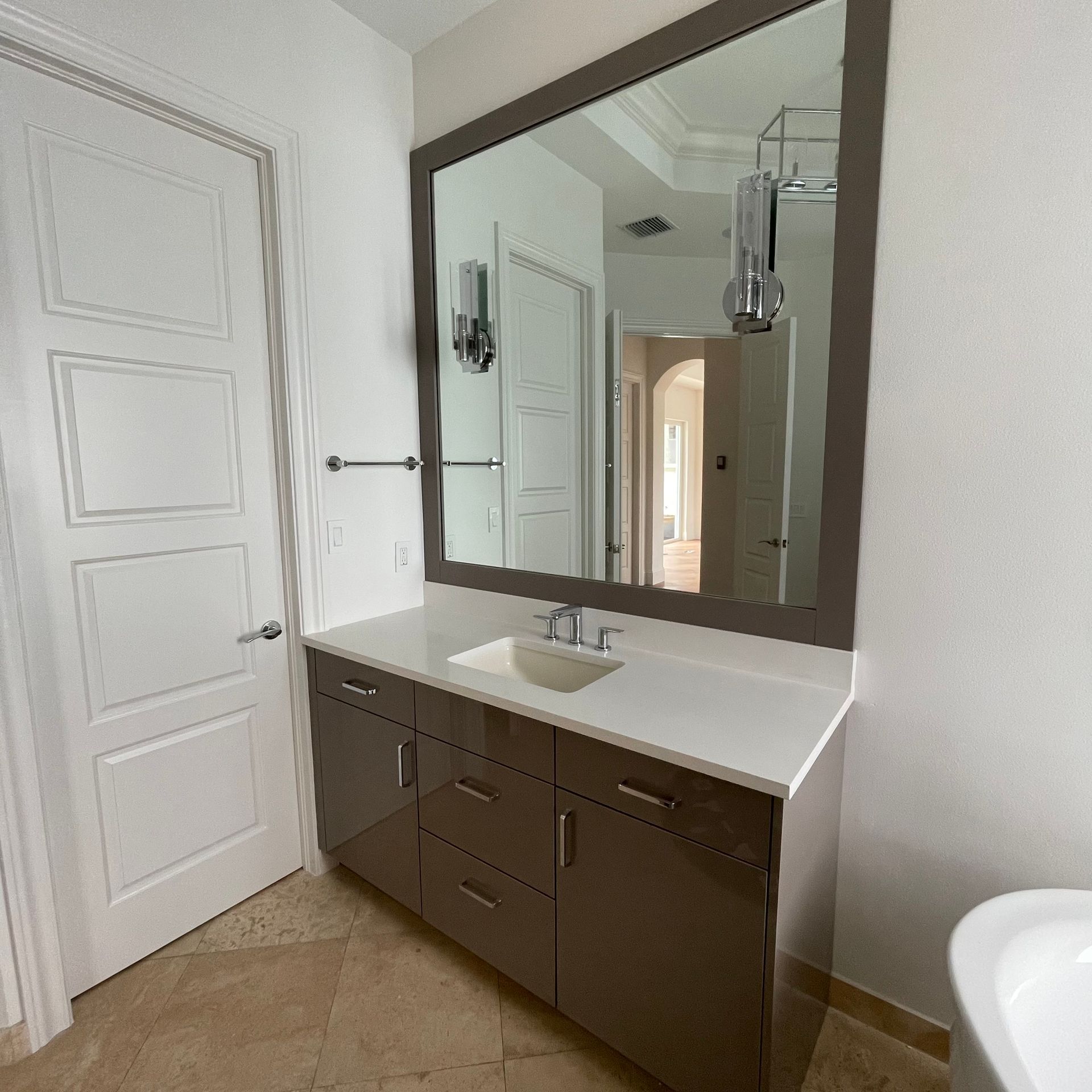 A bathroom vanity with a dark brown cabinet, white countertop, rectangular sink, and a large mirror on a white wall.