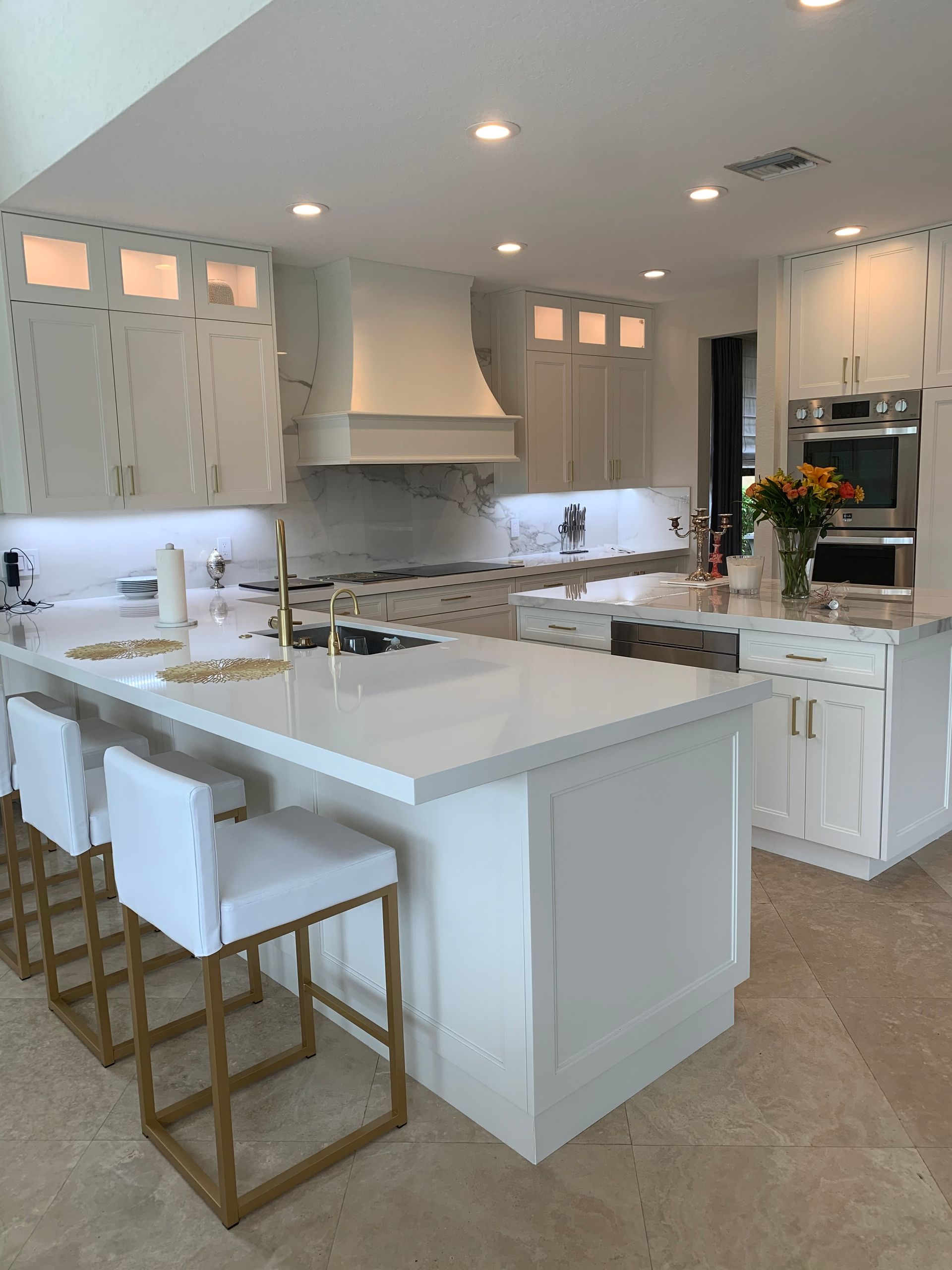A bright, modern kitchen featuring white cabinets, a large center island with white stools, and stainless steel appliances.