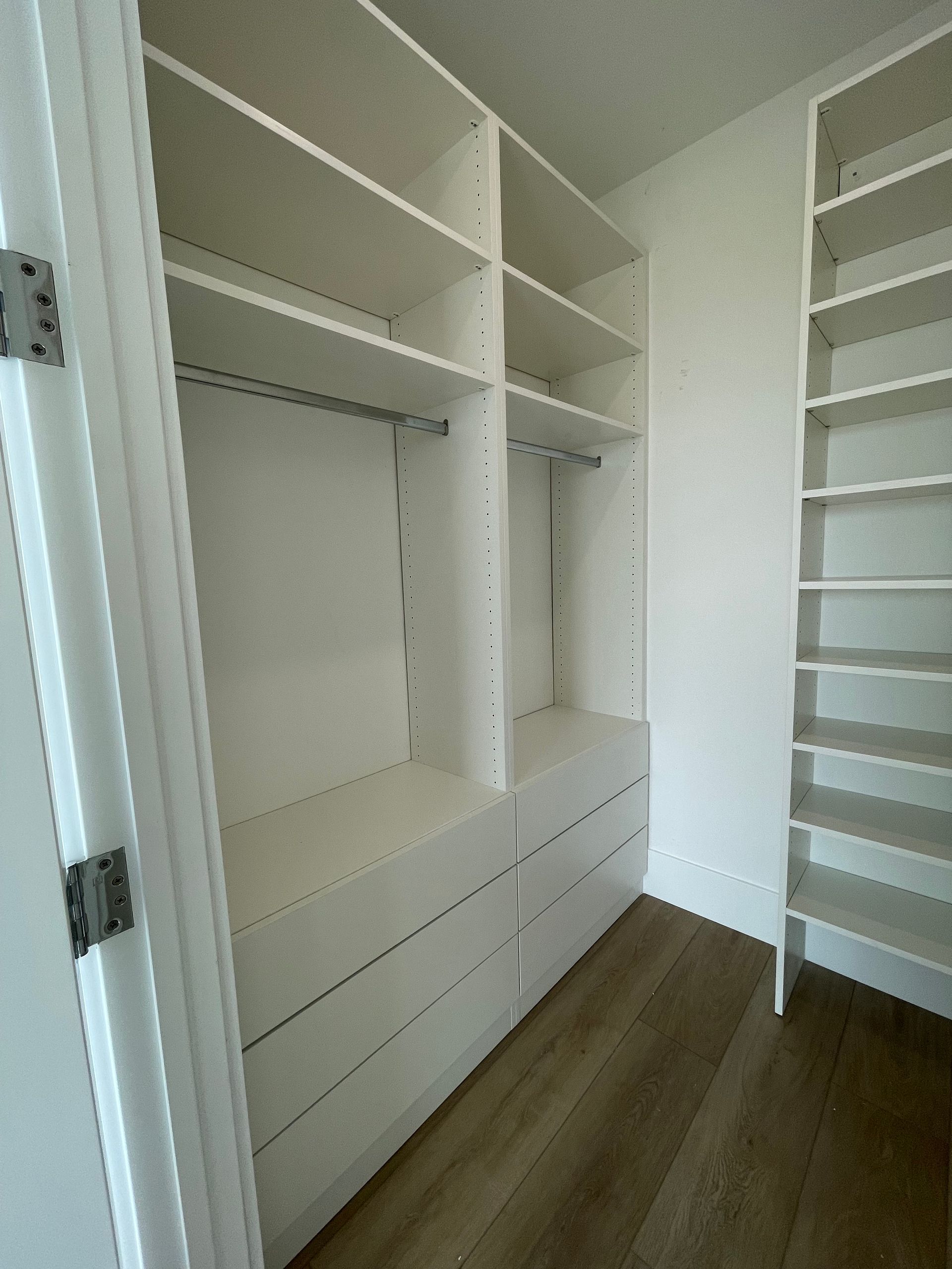 A walk-in closet featuring white wooden shelving, hanging rods, and built-in drawers over light wood-look flooring.