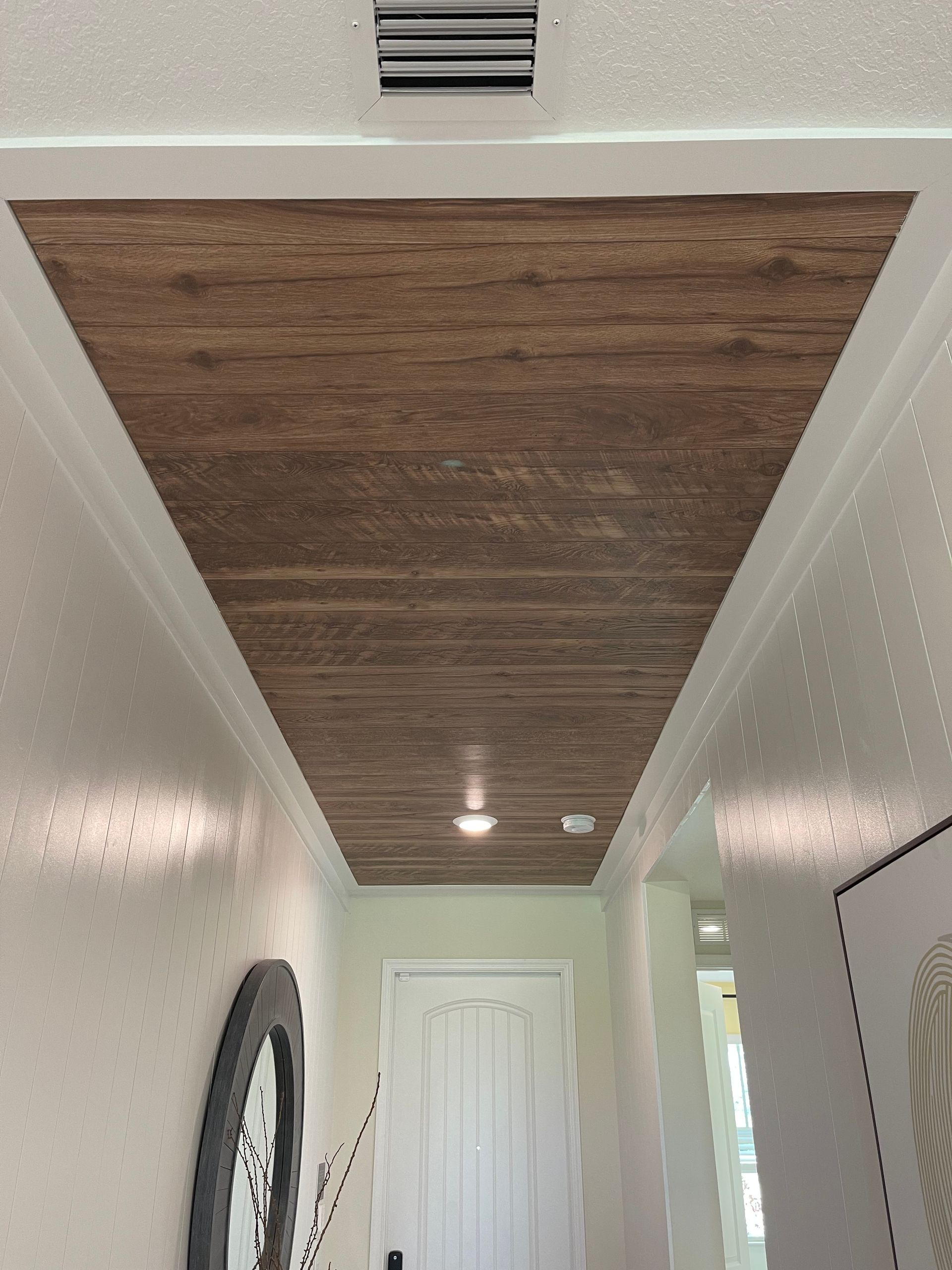 A hallway with white walls and a wood-paneled ceiling accent feature, illuminated by a recessed light.