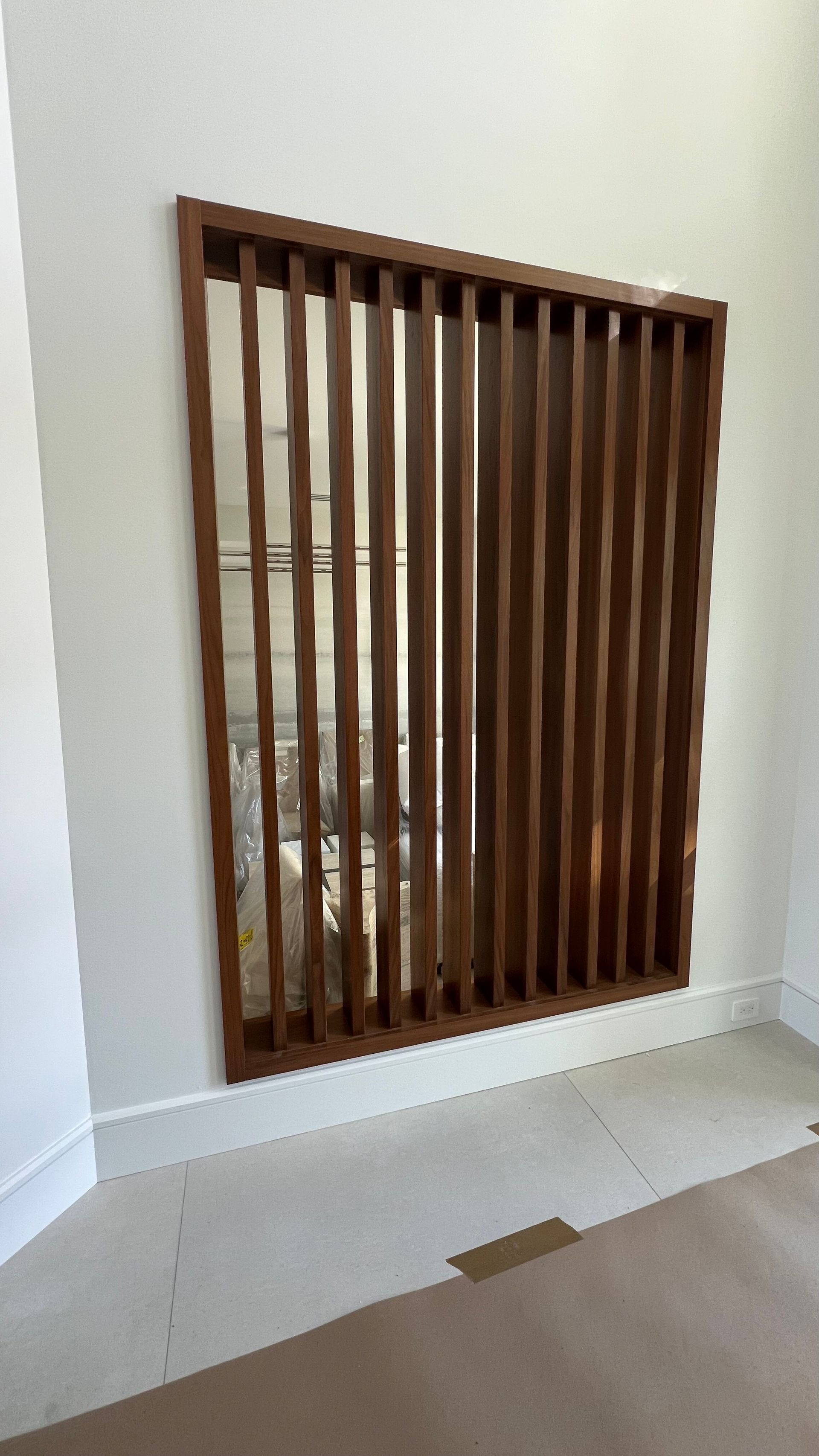 A wall-mounted decorative wooden slat screen with vertical panels, featuring a mirror reflection behind the slats.