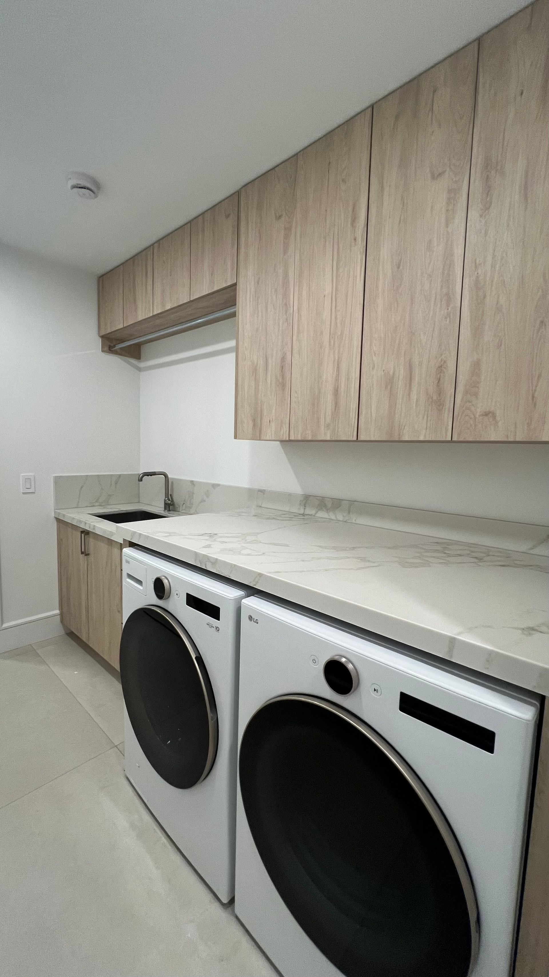 A laundry room featuring light wood cabinets, white stone countertops, and two white front-loading washing machines.