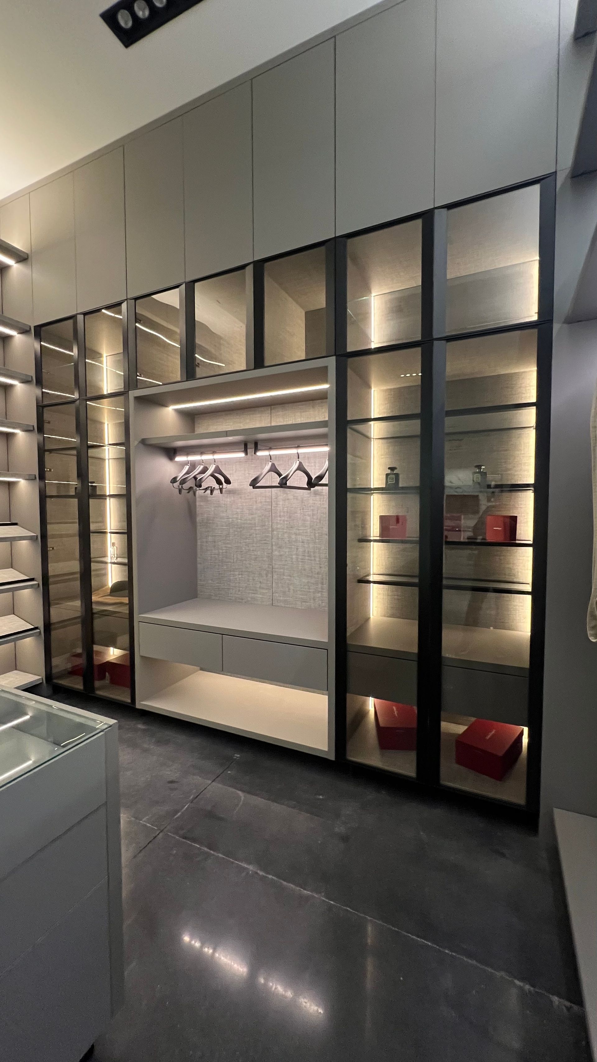 A modern, floor-to-ceiling wardrobe with illuminated glass-front cabinets and a central open hanging and drawer section.