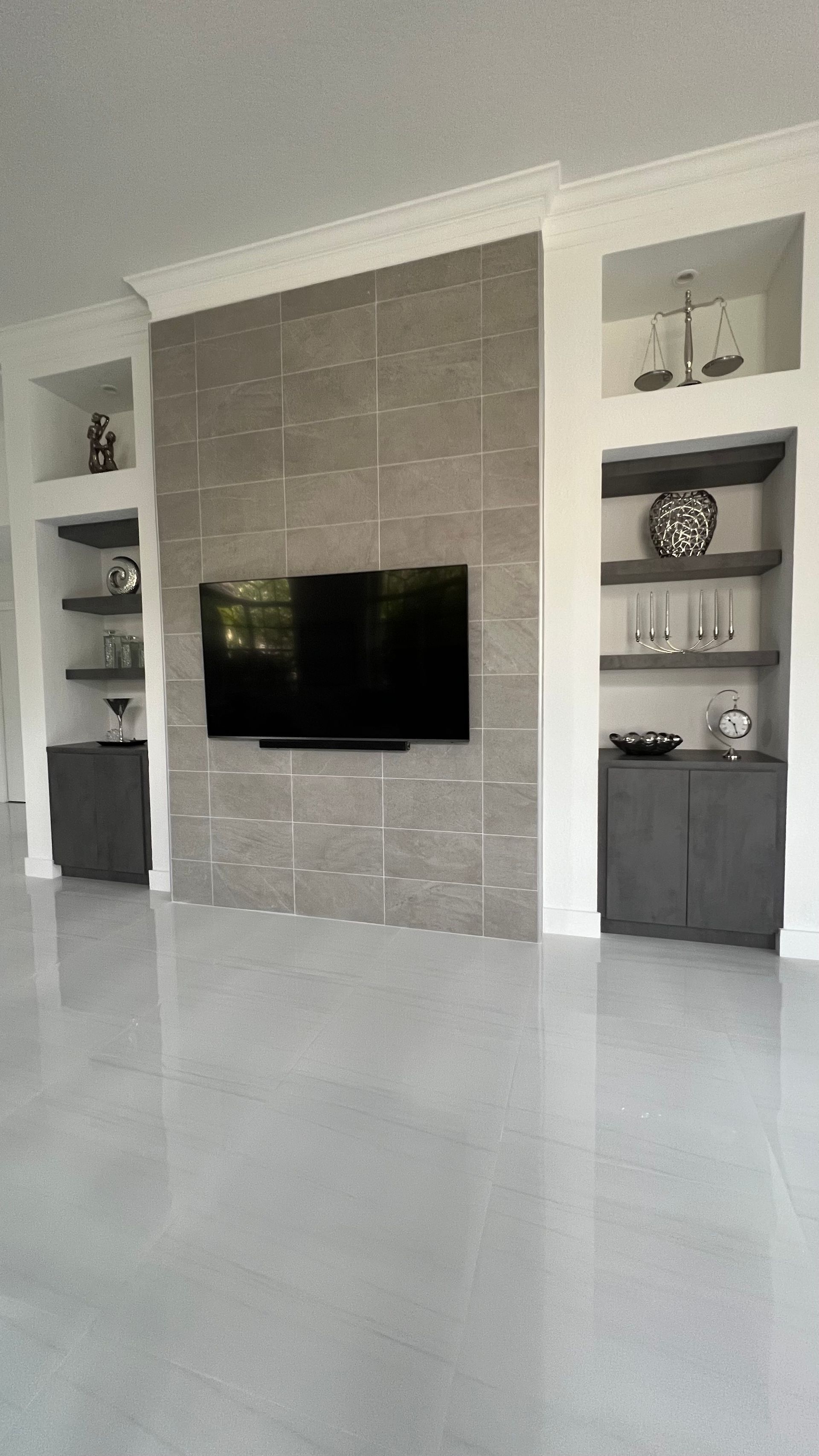 A wall-mounted TV on a textured gray stone accent wall, flanked by white built-in shelving and gray cabinets.