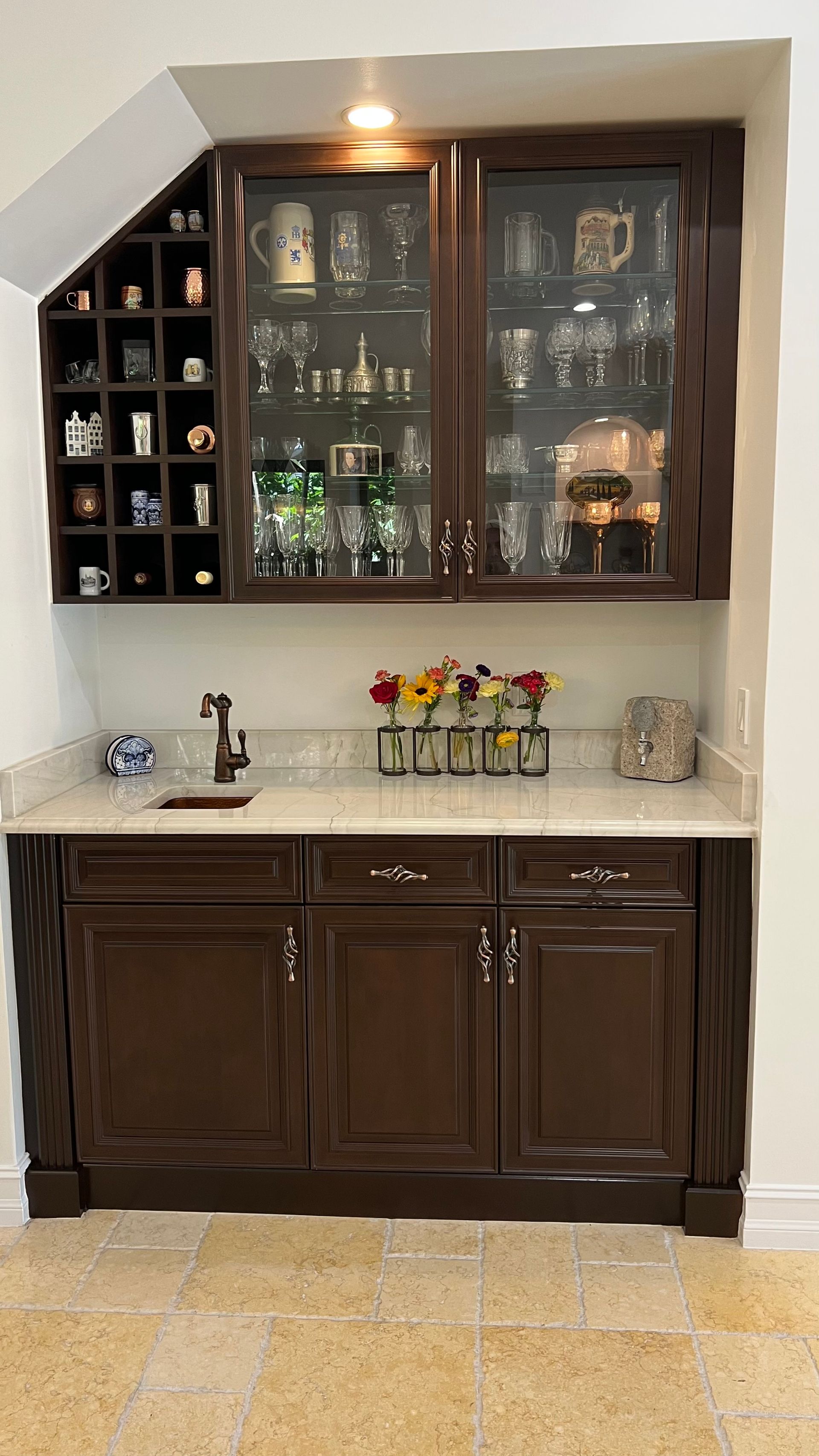 A built-in wet bar with dark wooden cabinets, glass-front upper storage, a stone countertop, and a small sink.