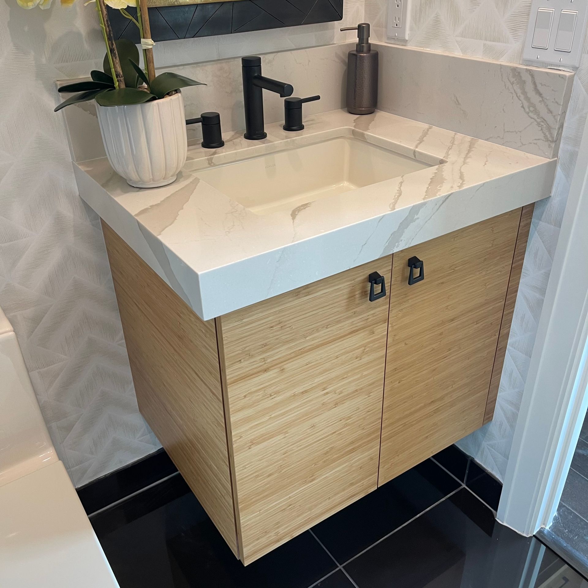 A floating wooden bathroom vanity with a white marble countertop, black fixtures, and a small potted plant.