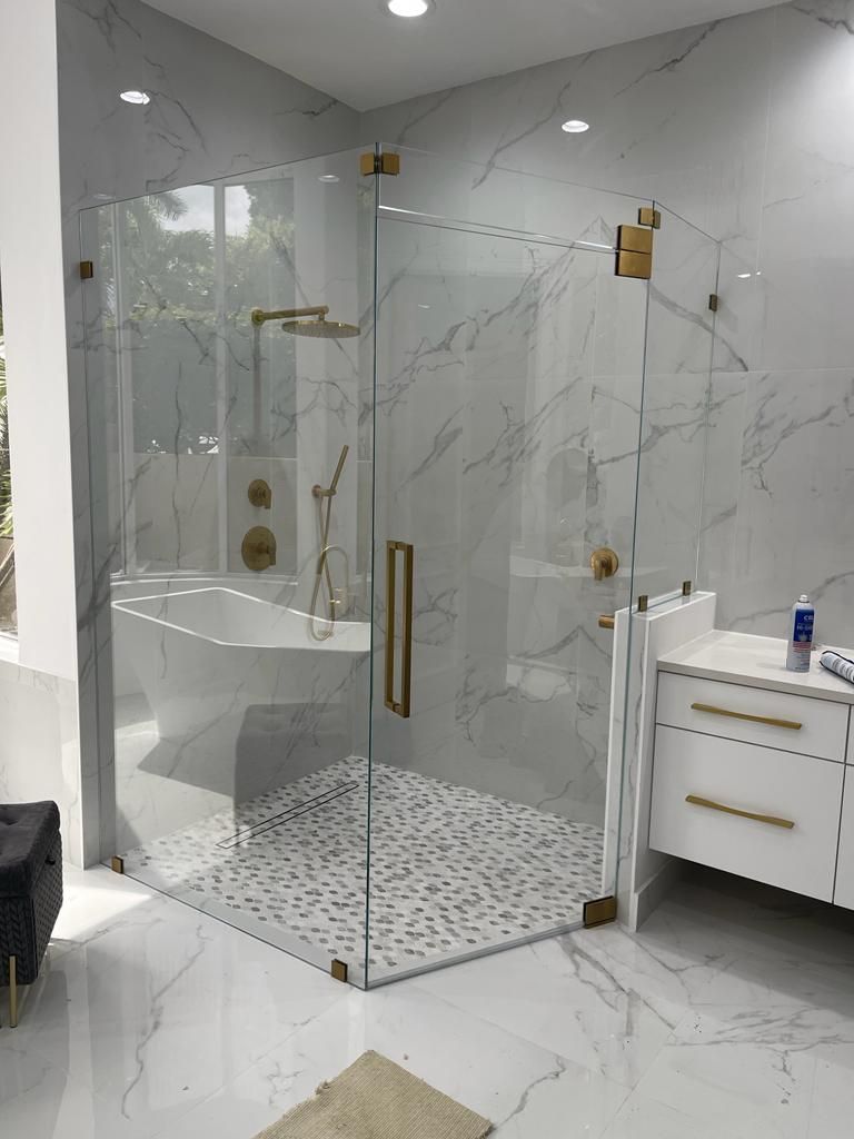 Modern bathroom with a glass-enclosed shower, gold hardware, marble-patterned walls and floor, and a white vanity.