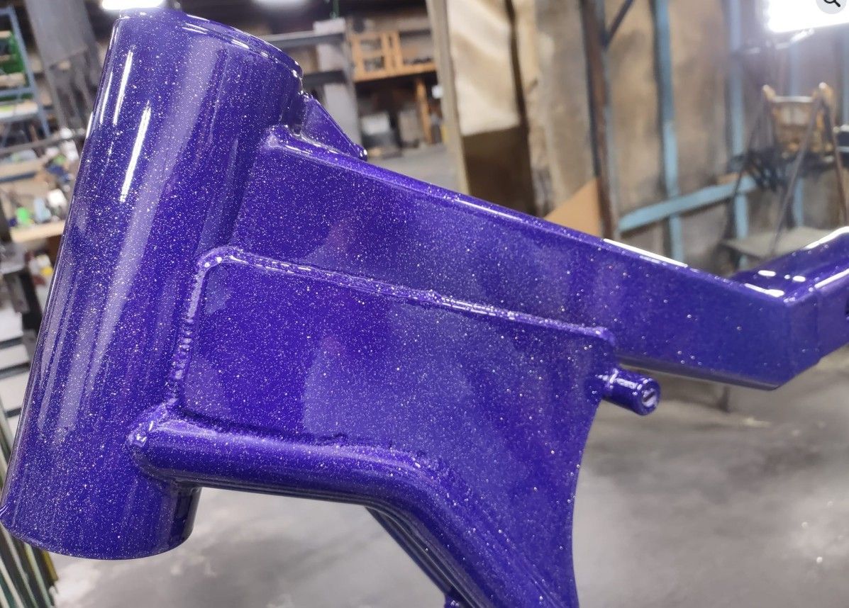 A purple motorcycle frame is sitting on the floor