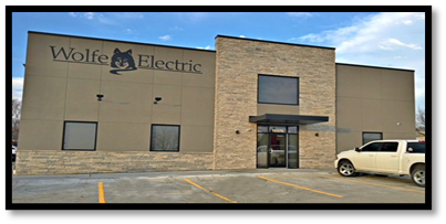 A white truck is parked in front of a building that says wolfe electric.