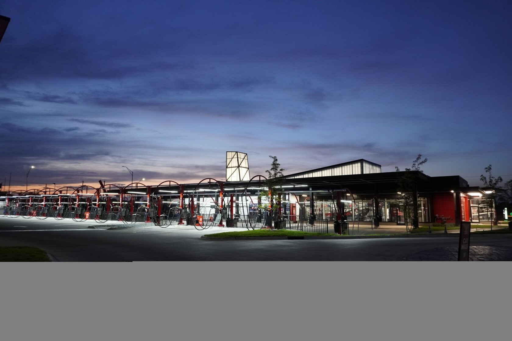 A car wash is lit up at night with a blue sky in the background.