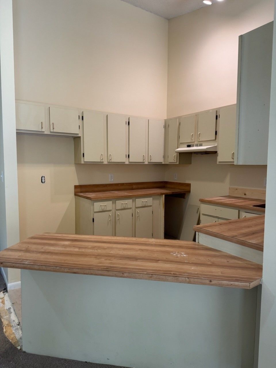 Before image of kitchen with white cabinets and a wooden counter top.