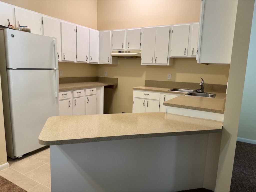 After image of kitchen with white cabinets, a refrigerator and a sink.