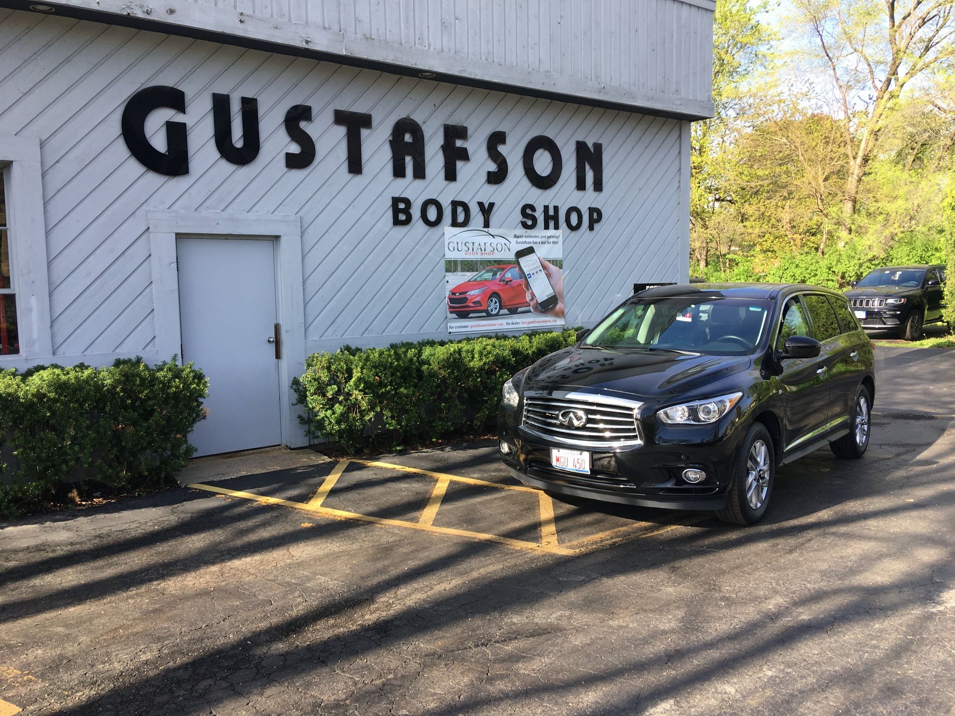 Black SUV parked in front of Gustafson Body Shop; sign on building.