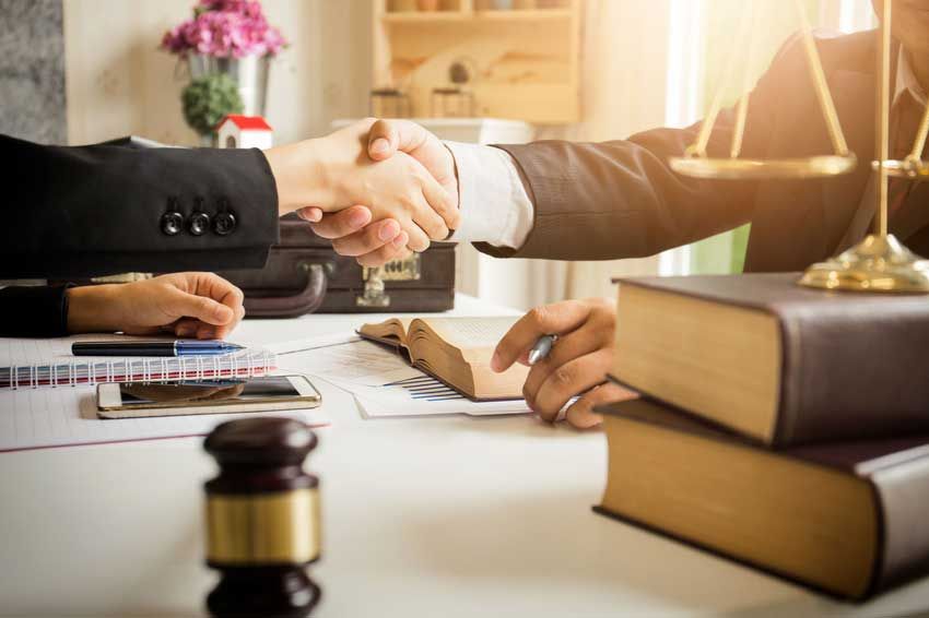 A lawyer is shaking hands with a client in front of a scale of justice.