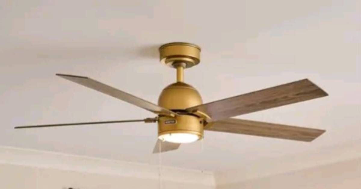 Gold ceiling fan with five wooden blades, mounted on a white ceiling.