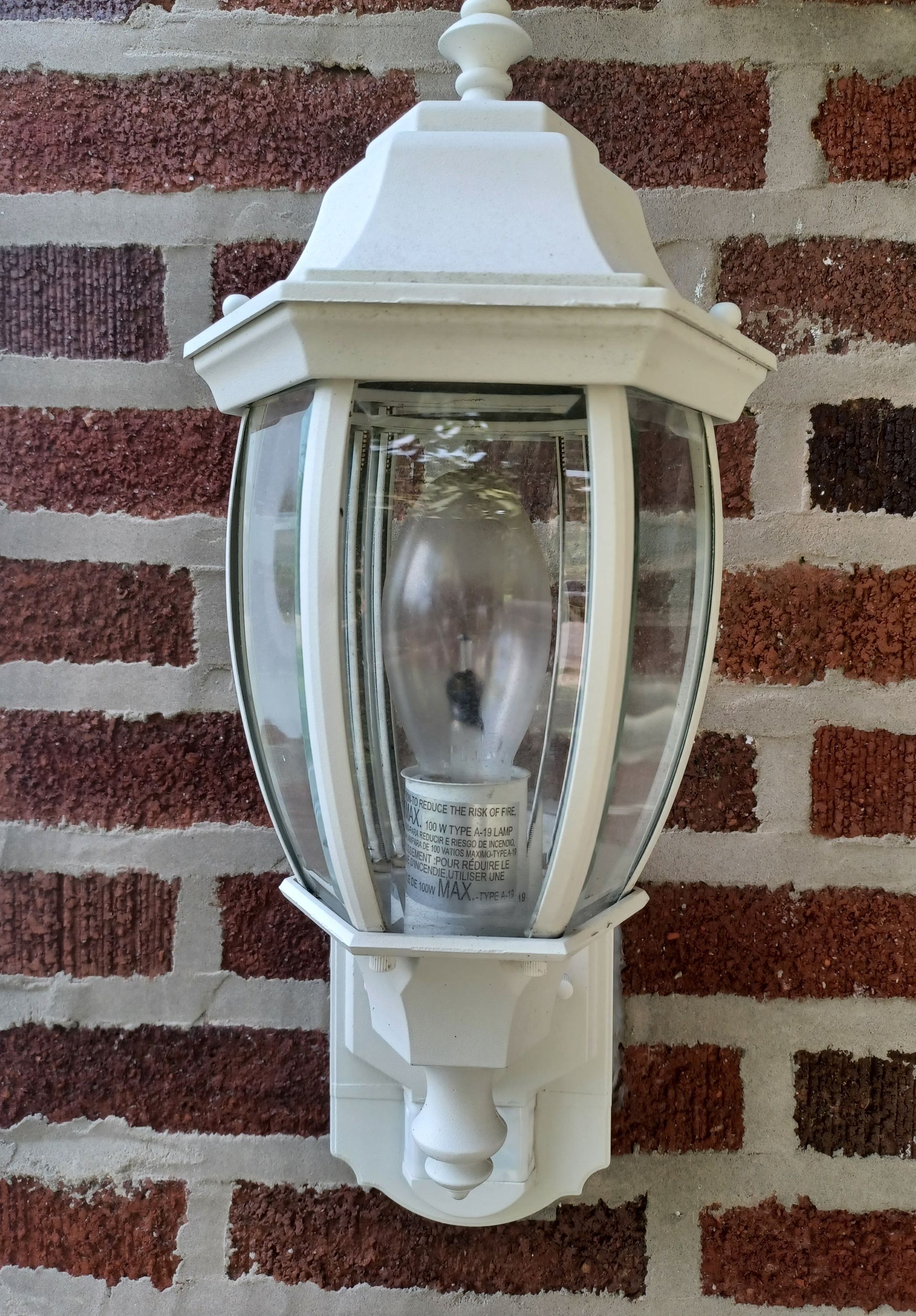A white light fixture is hanging on a brick wall