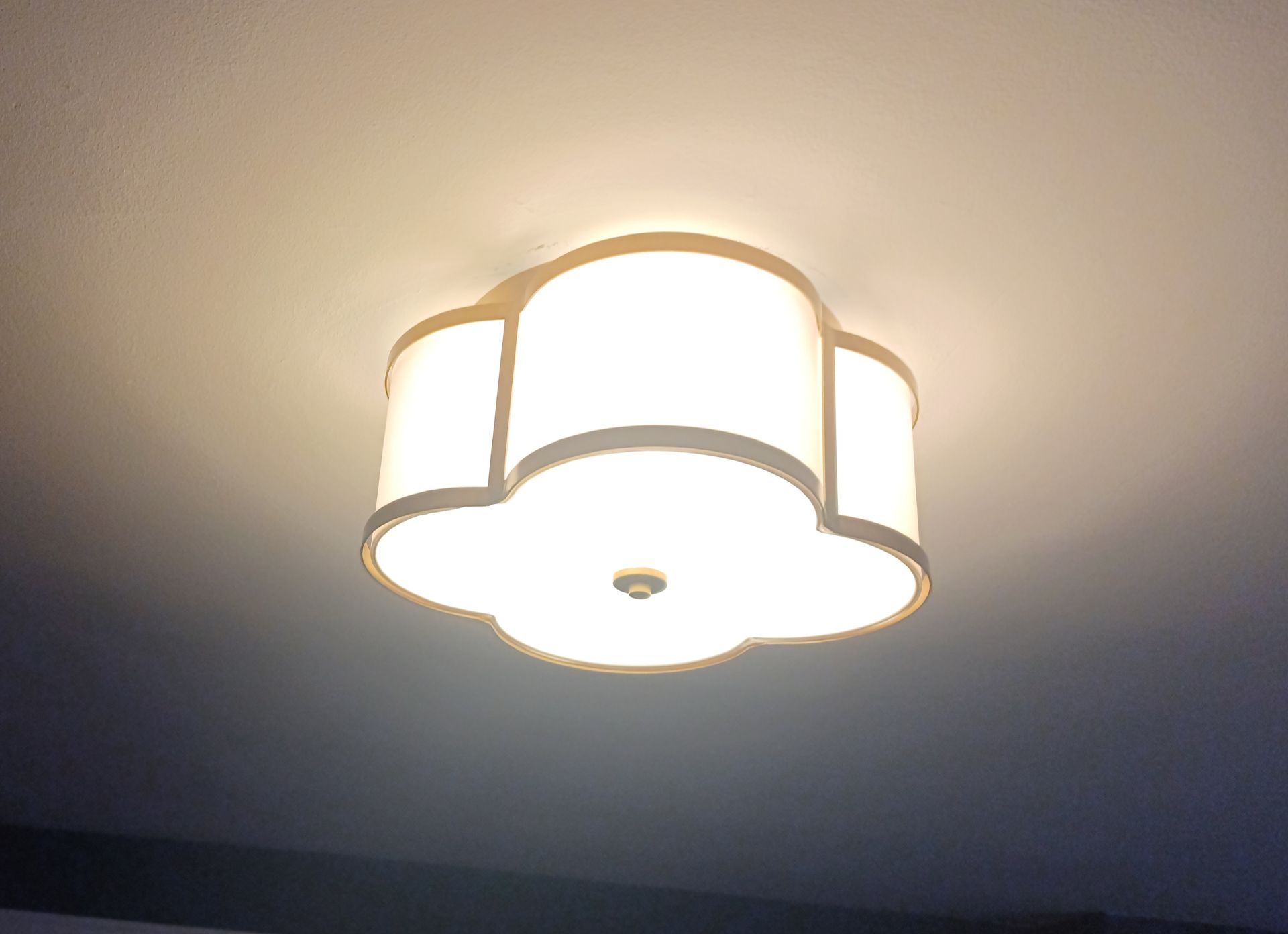 A white, floral-shaped ceiling light fixture illuminates a room, casting a warm glow on the white ceiling.