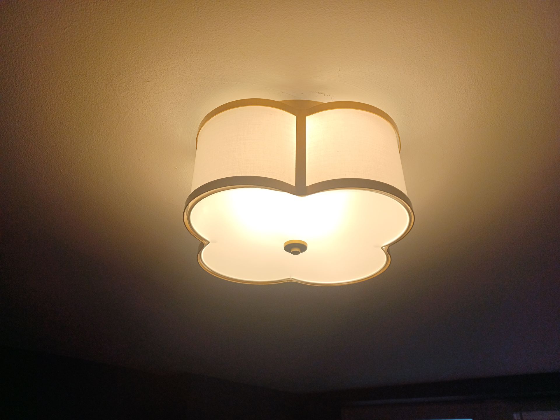 Ceiling-mounted light fixture with a floral-shaped shade, illuminated, casting light on the ceiling.