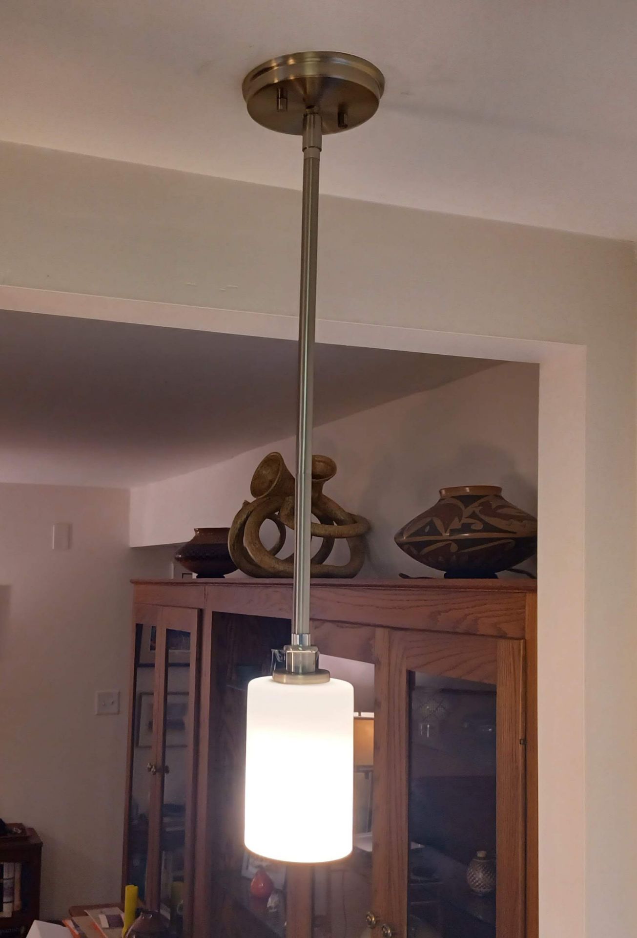 A cylindrical pendant light hangs from the ceiling; a wooden cabinet with art objects is visible in the background.