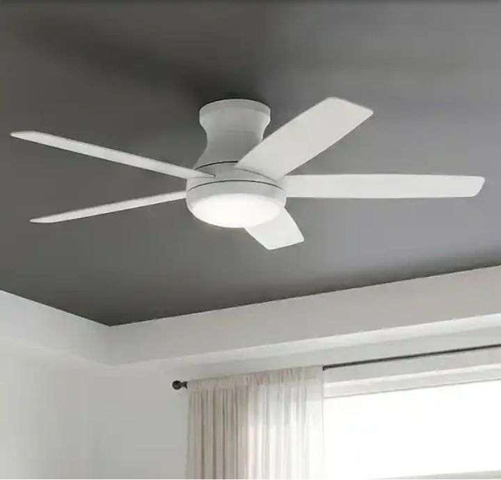 White ceiling fan with five blades on a dark ceiling above a window with sheer curtains.