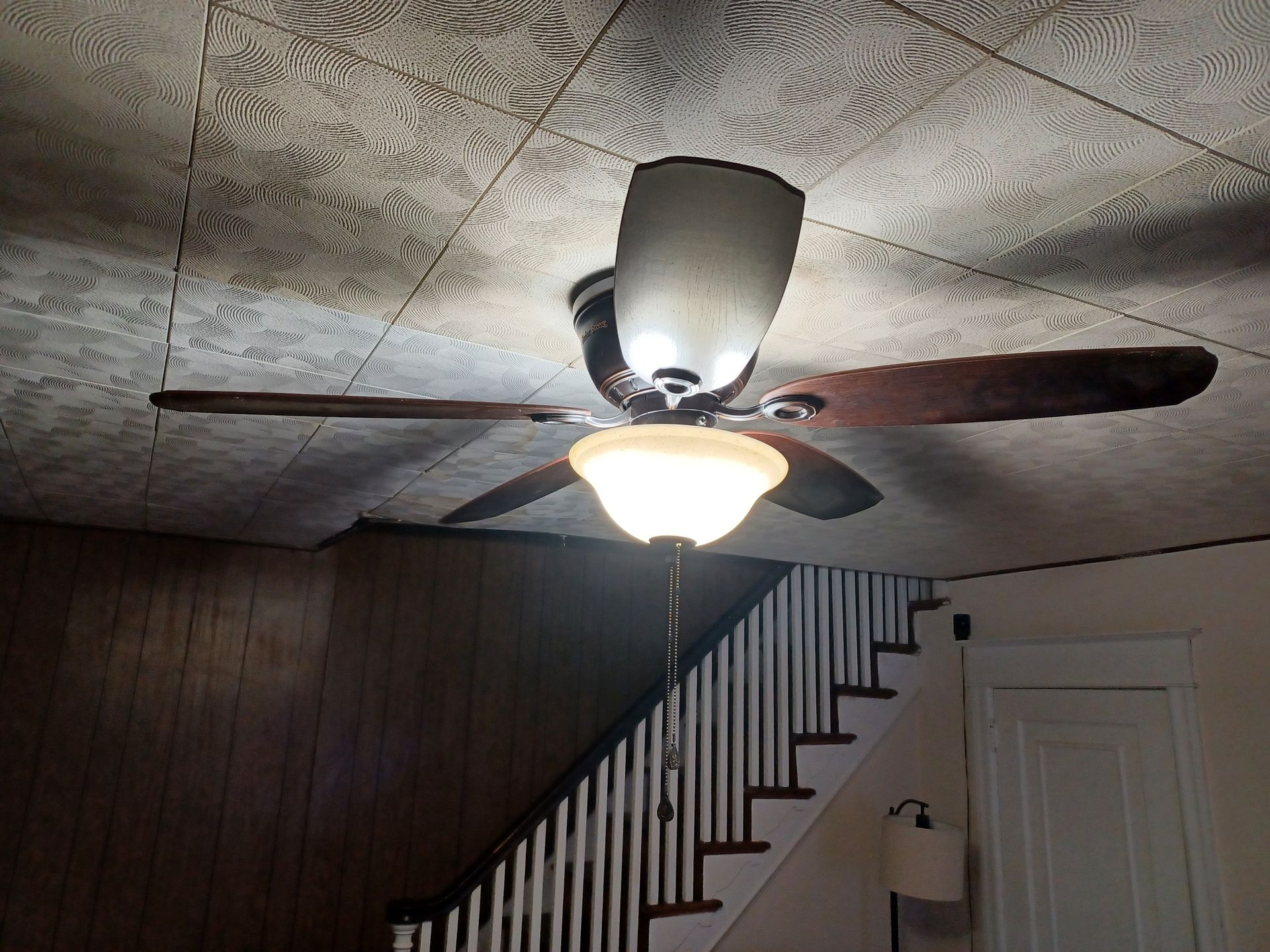 A ceiling fan is hanging from the ceiling of a room next to a staircase.