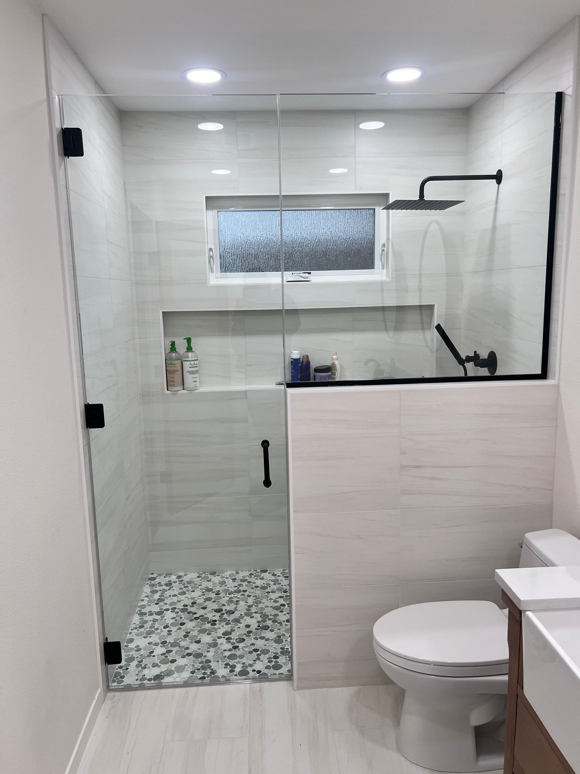 Modern bathroom with glass shower enclosure, white tiles, pebble floor, and toilet.