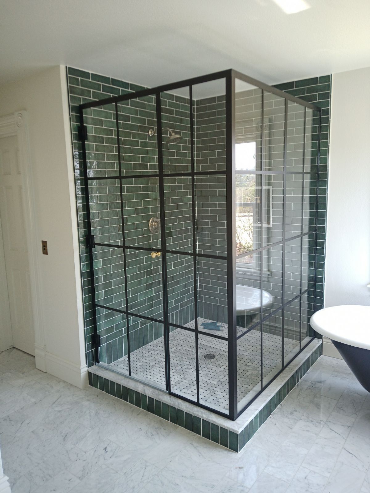 Green tiled shower enclosure with black grid frame, glass panels, and patterned floor.