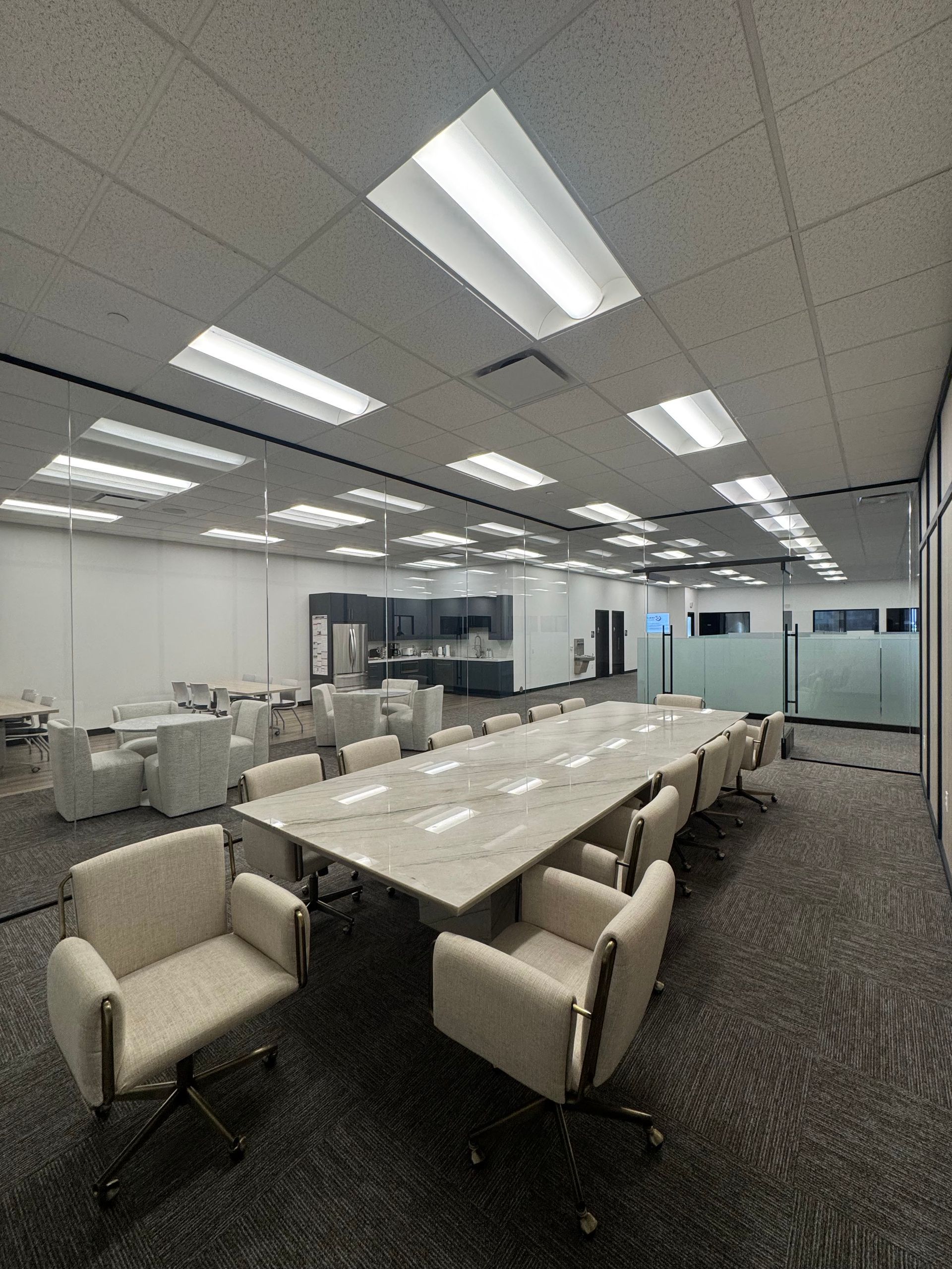 Conference room with long table, cream chairs, and ceiling lights; a modern office space.