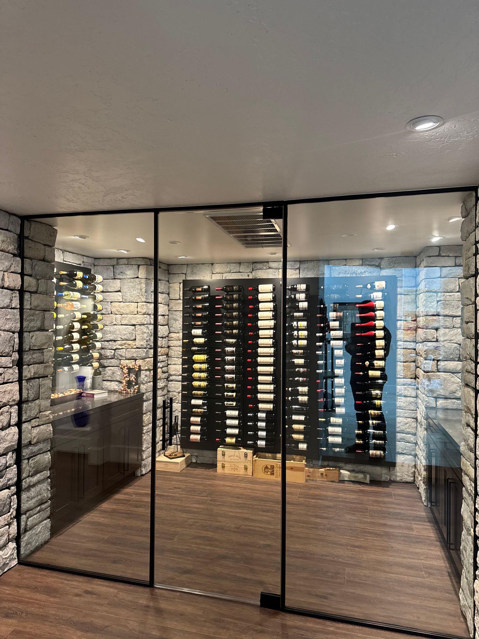Wine cellar with glass door, stone walls, and bottles on shelves. A person is visible inside.