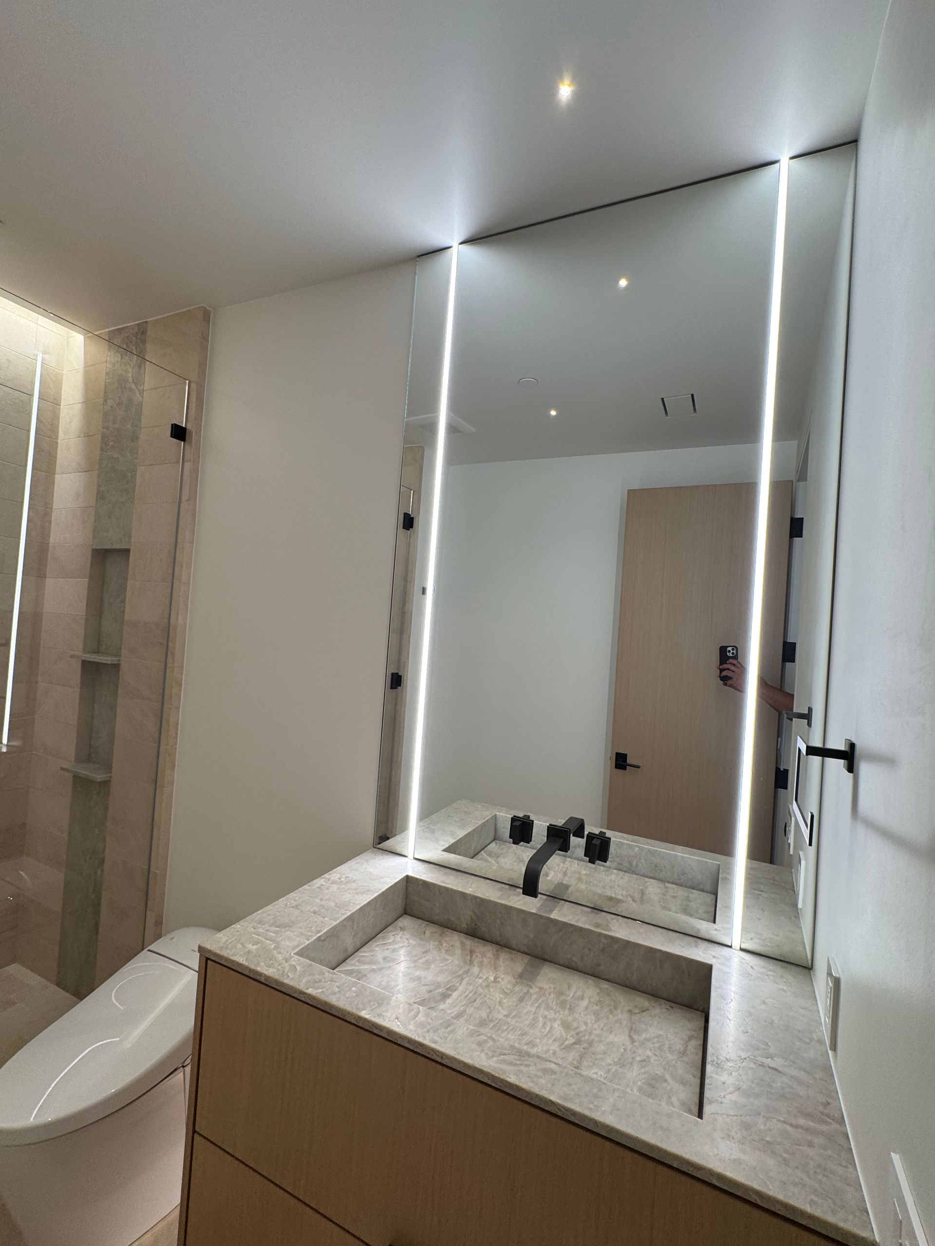 Modern bathroom with large mirror and integrated lighting above a countertop sink and toilet.